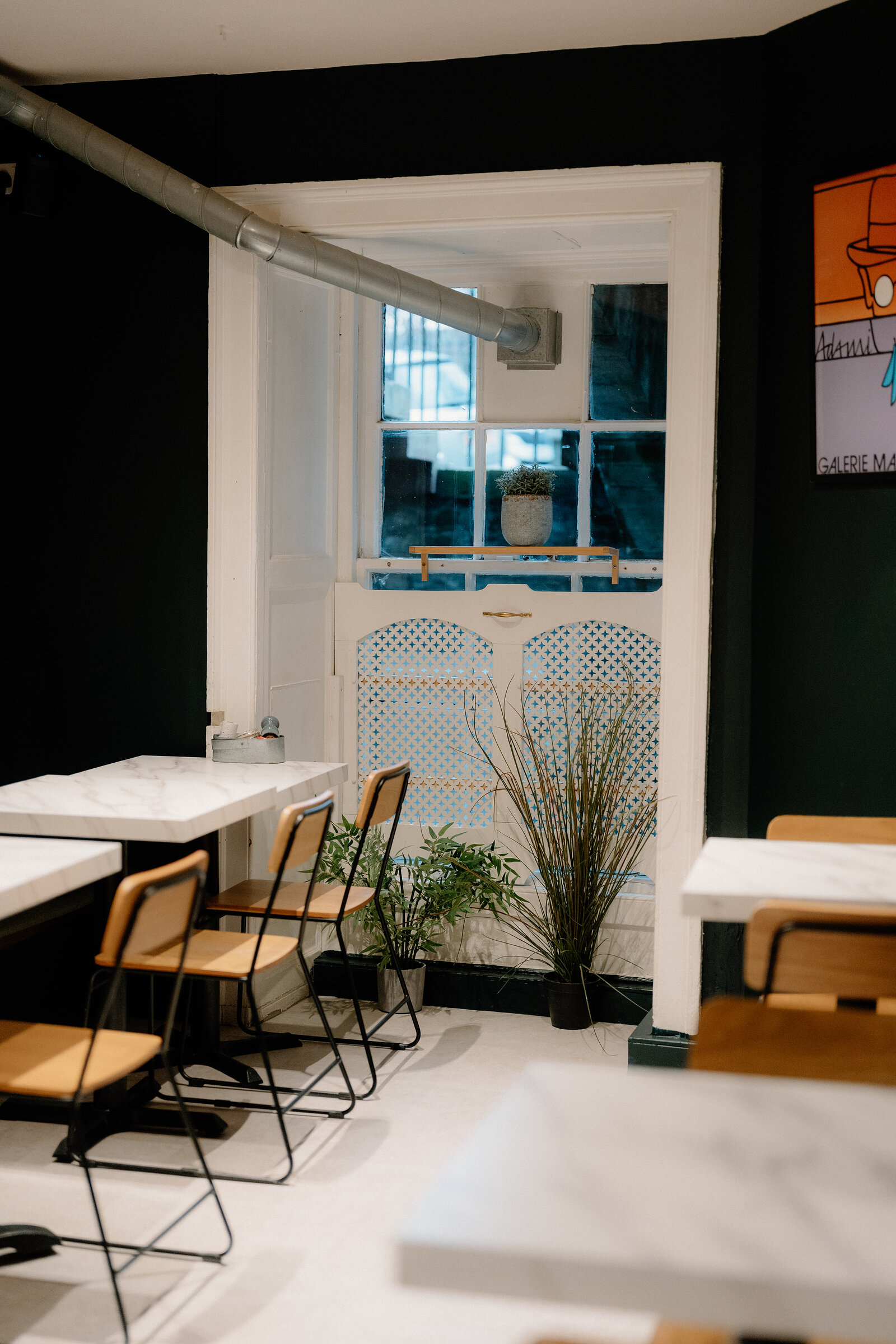 Marble-topped tables sit before a black wall and an arched window with a lattice screen beyond.