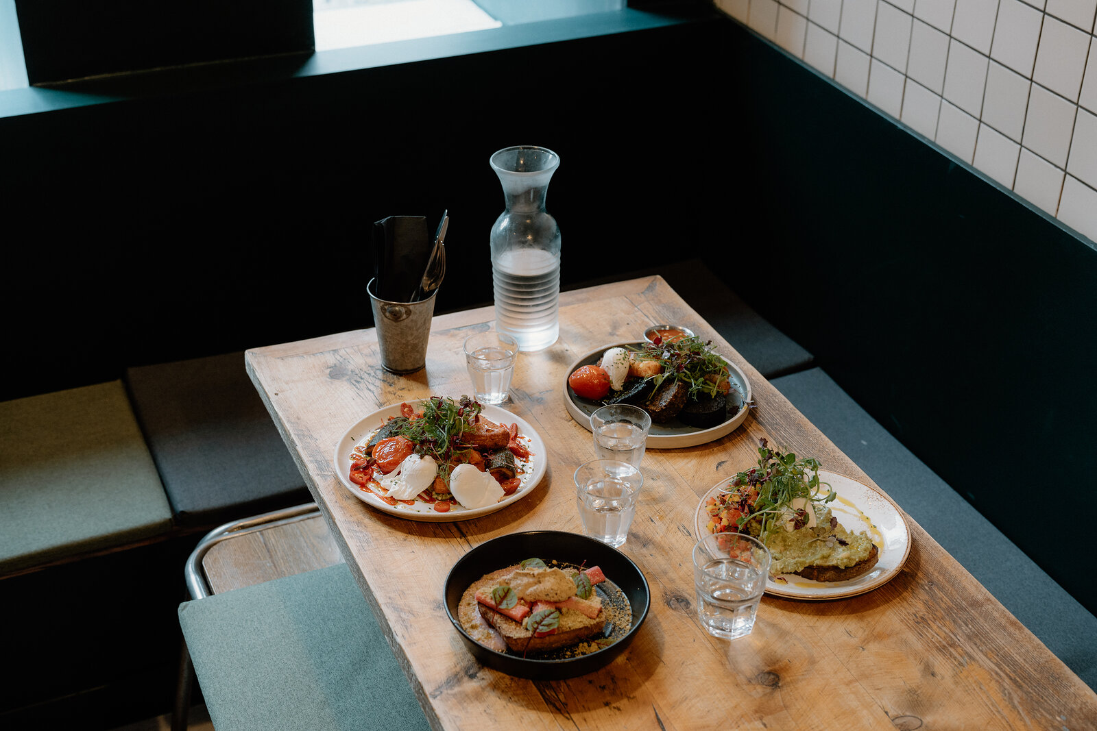Plates of brunch dishes and a water carafe are set on a wooden table beside a booth.