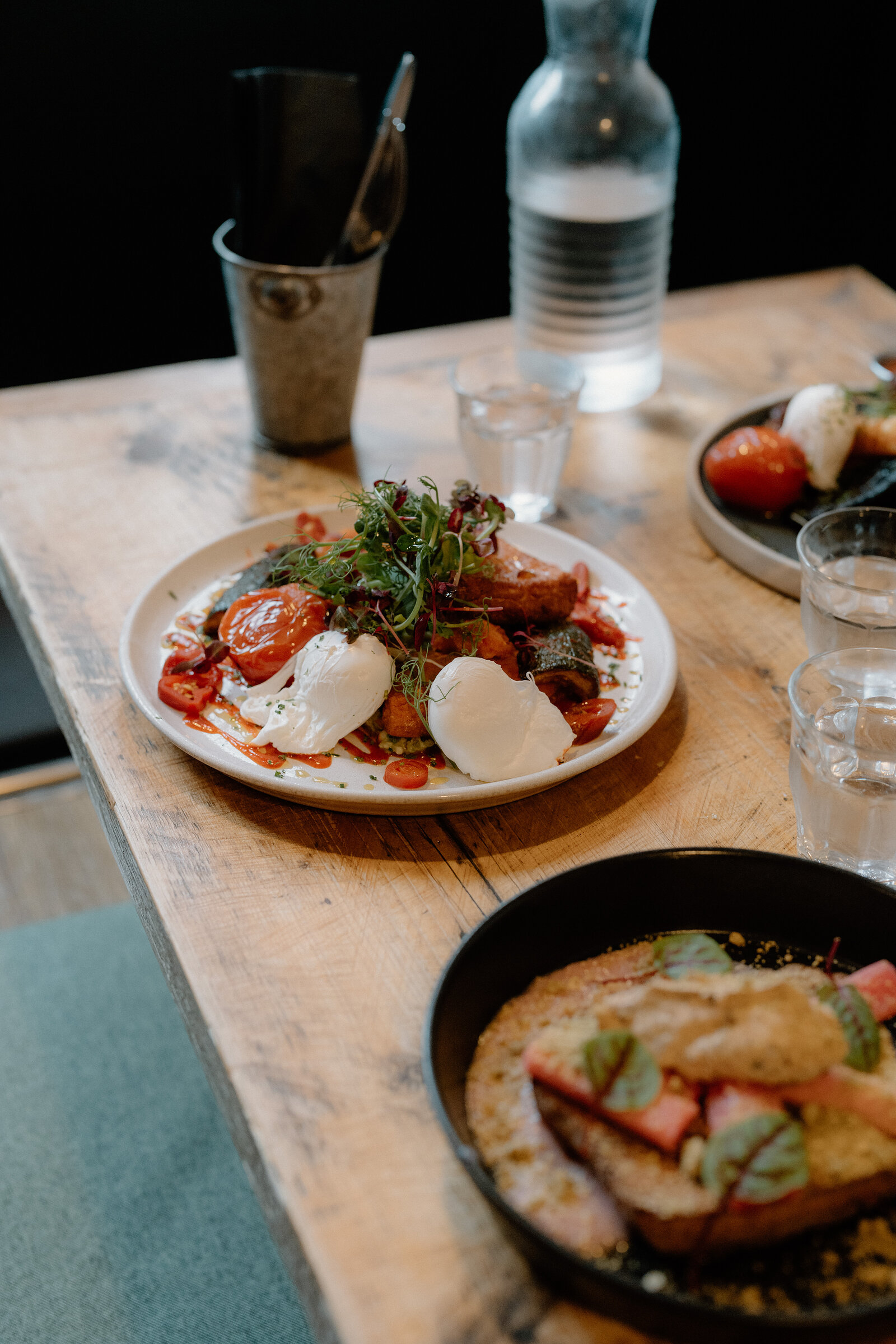Plates of poached eggs, burrata and toasted bread with rhubarb sit together on a wooden table.