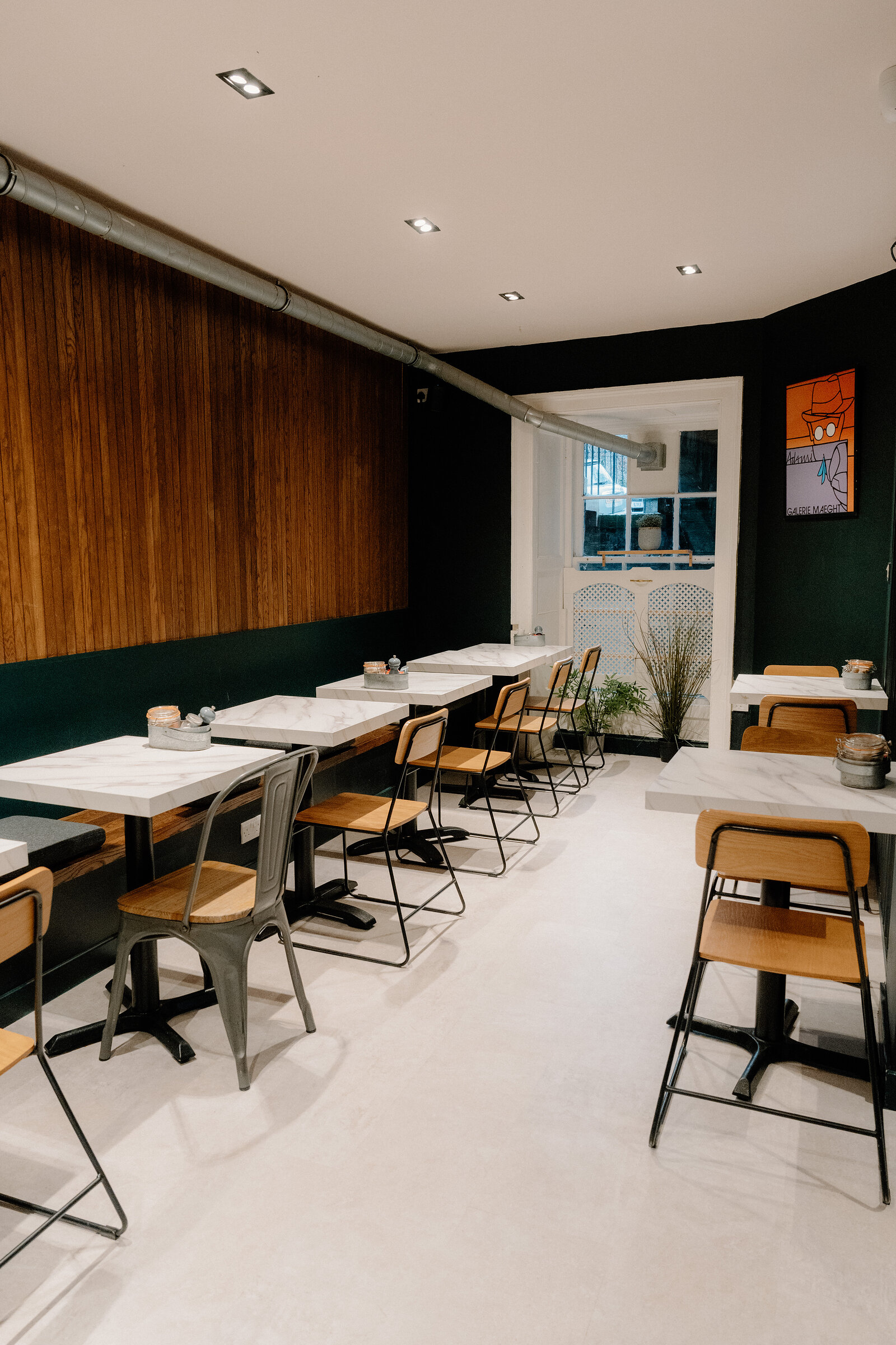 Marble-topped tables and mismatched chairs sit before a dark green wall and wood-panelled feature wall.