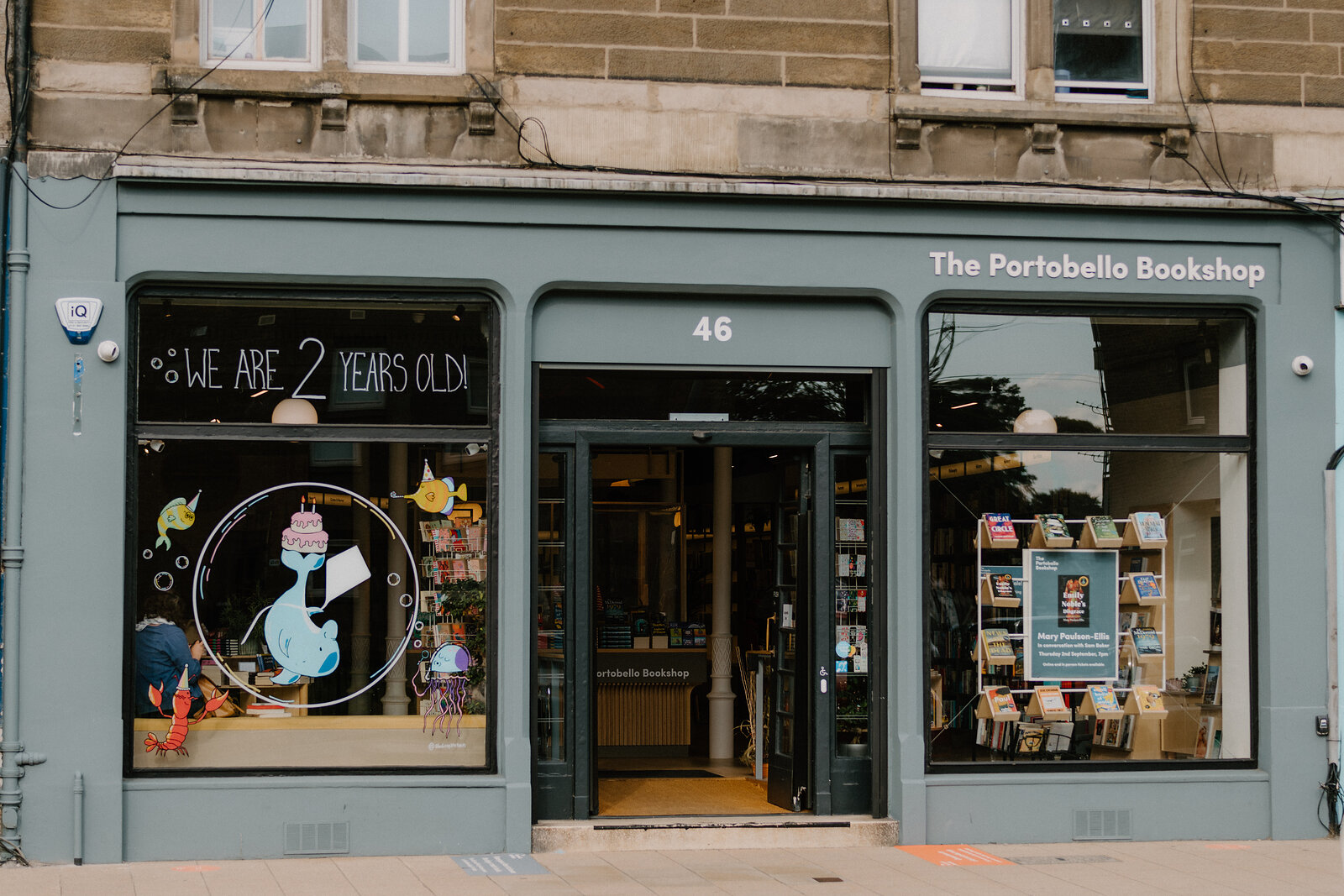 The Portobello Bookshop's green shopfront displays books behind its windows on a sandstone street.