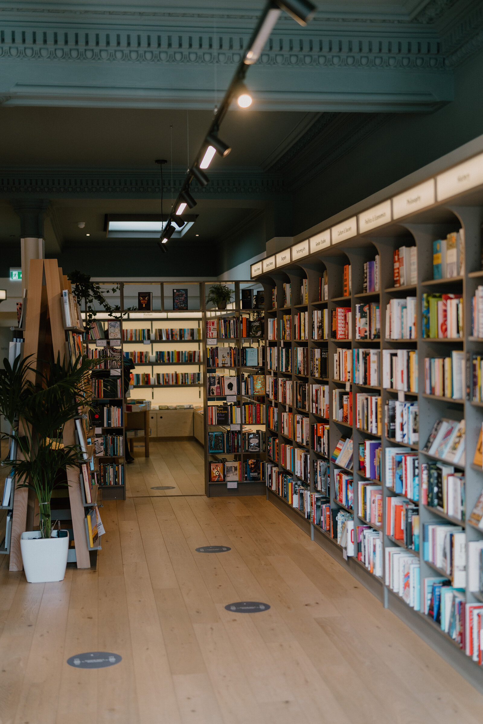 Tall bookshelves line an aisle in The Portobello Bookshop beneath an ornate ceiling.