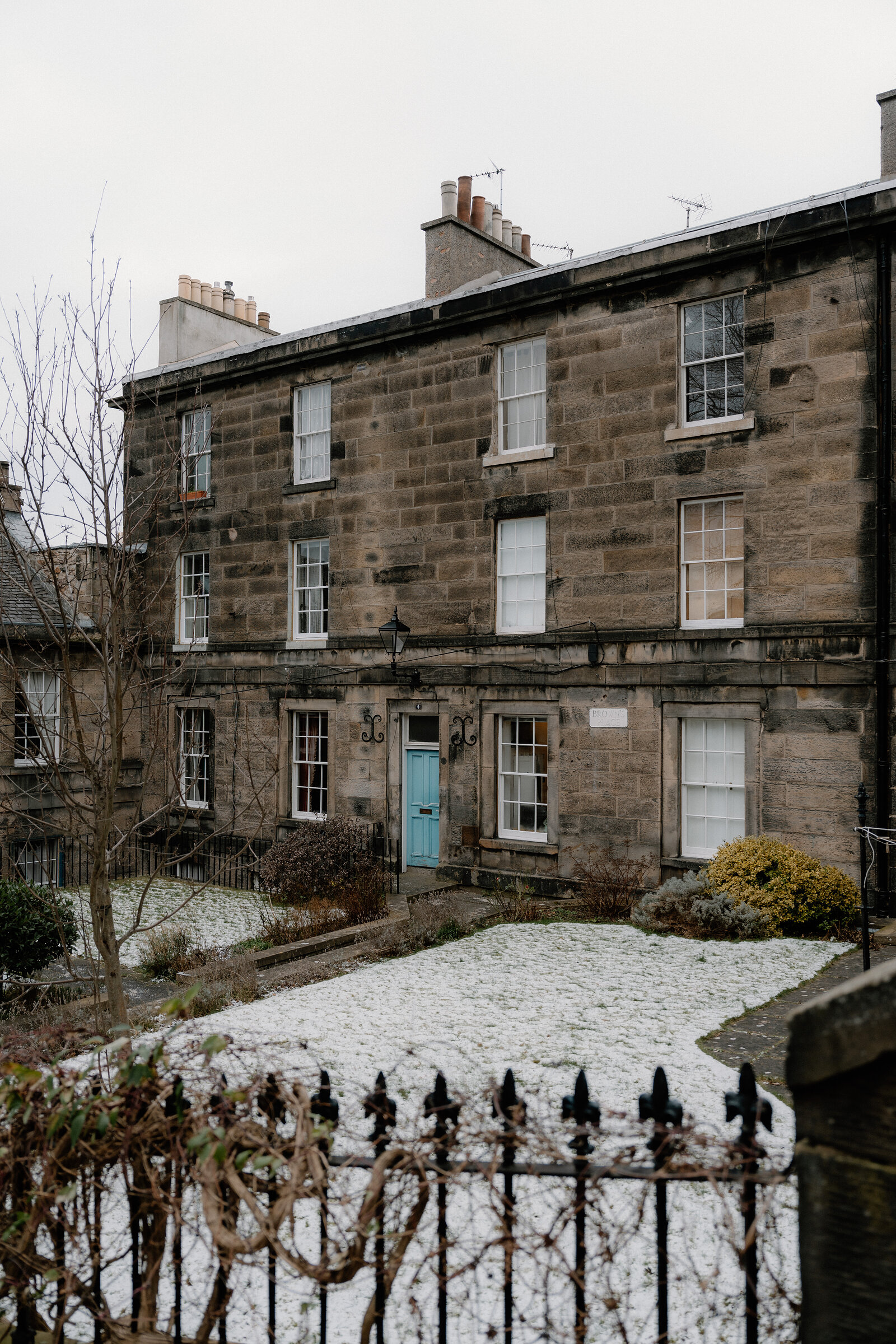 A snow-dusted Georgian tenement with a teal door stands behind an iron railing.