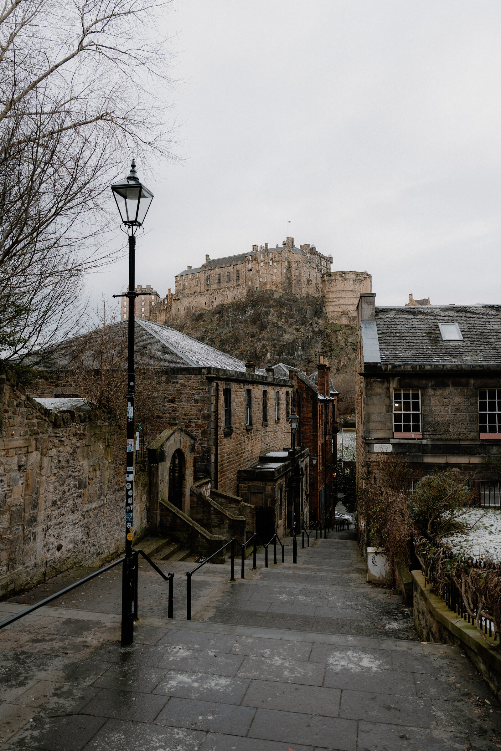 A lamppost and stepped path lead down toward Edinburgh Castle rising above rooftops.