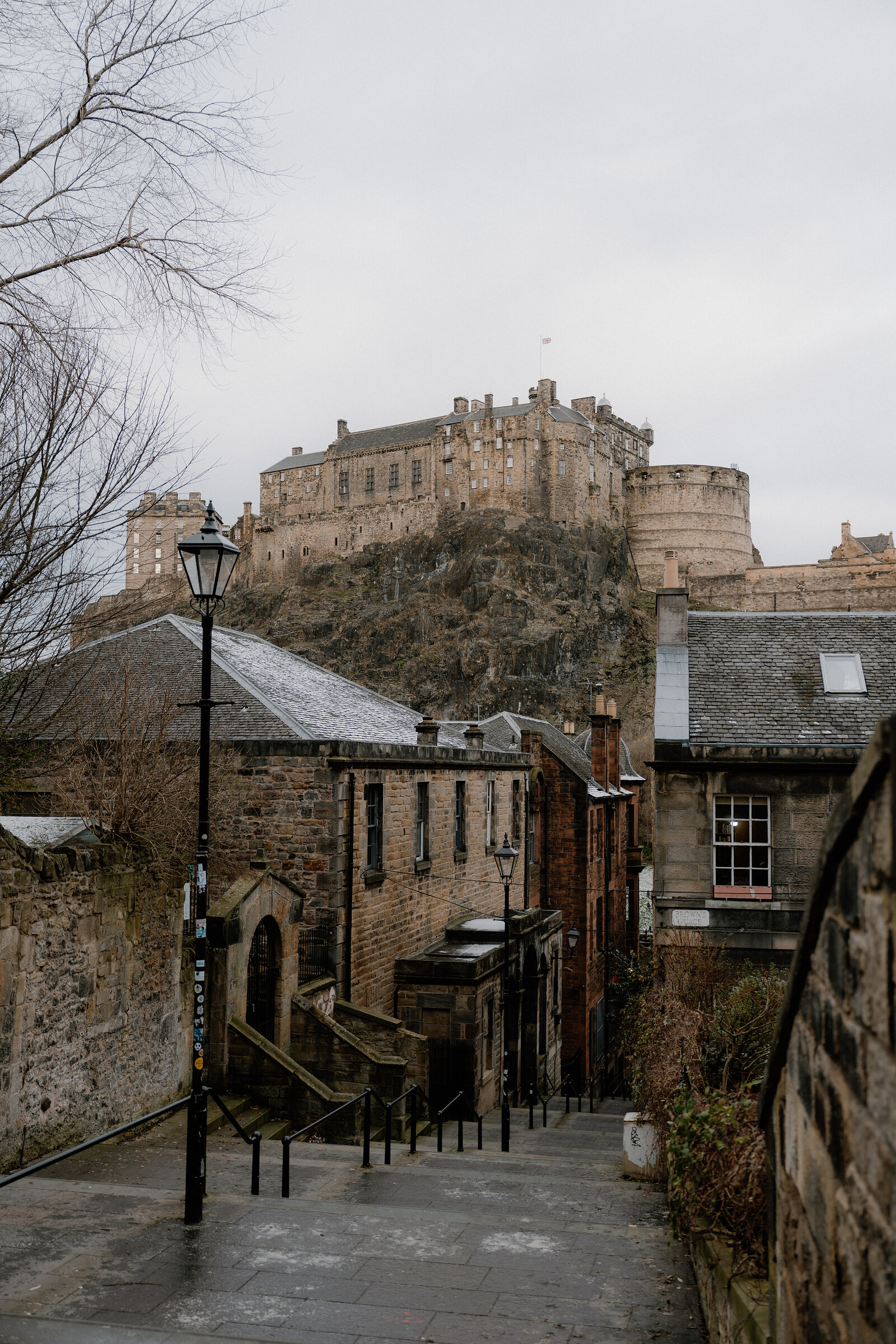 A stepped lane with a lamppost leads down past sandstone buildings toward Edinburgh Castle.
