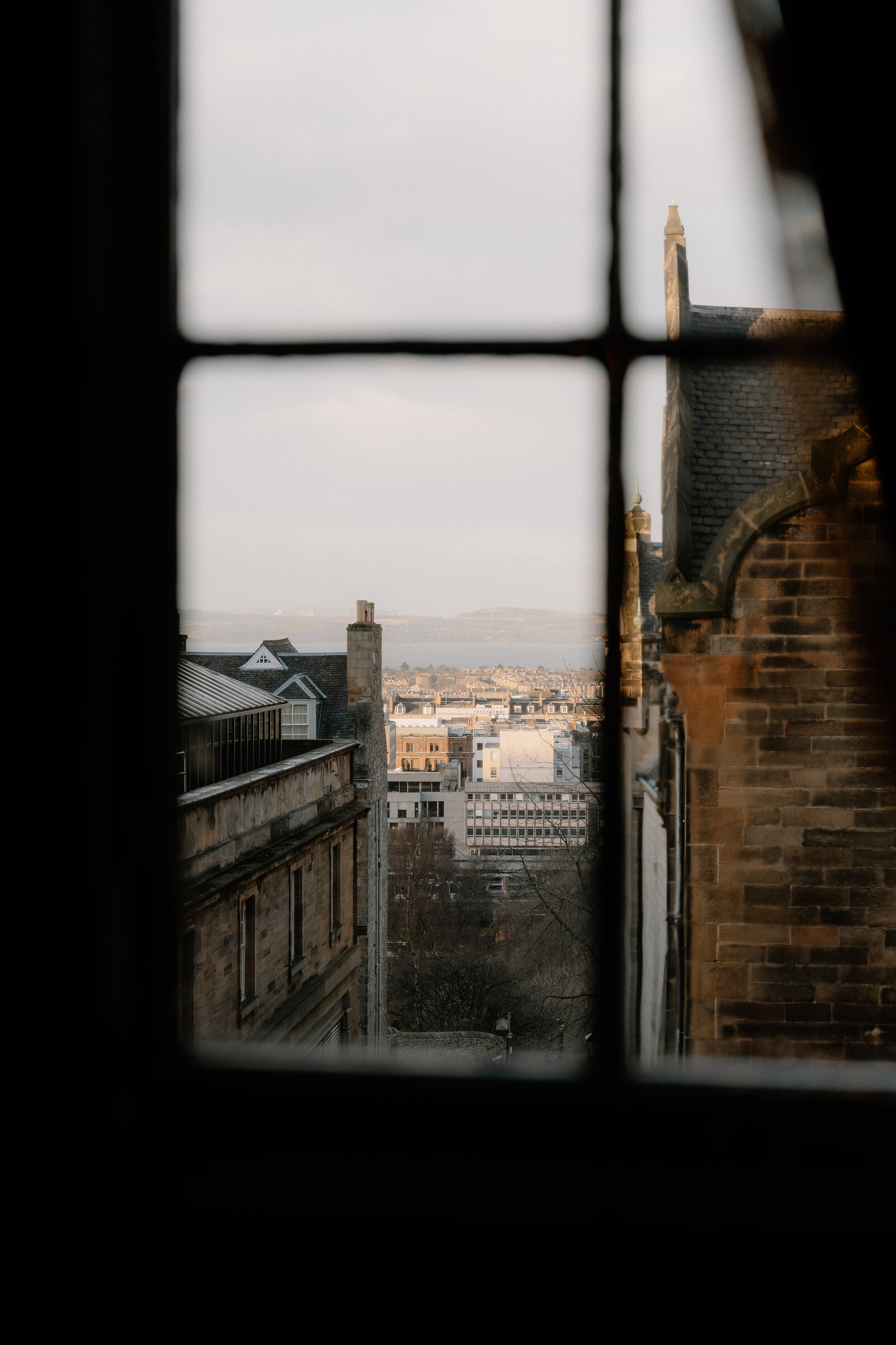 A church spire and rooftops are seen through a sash window overlooking Edinburgh.