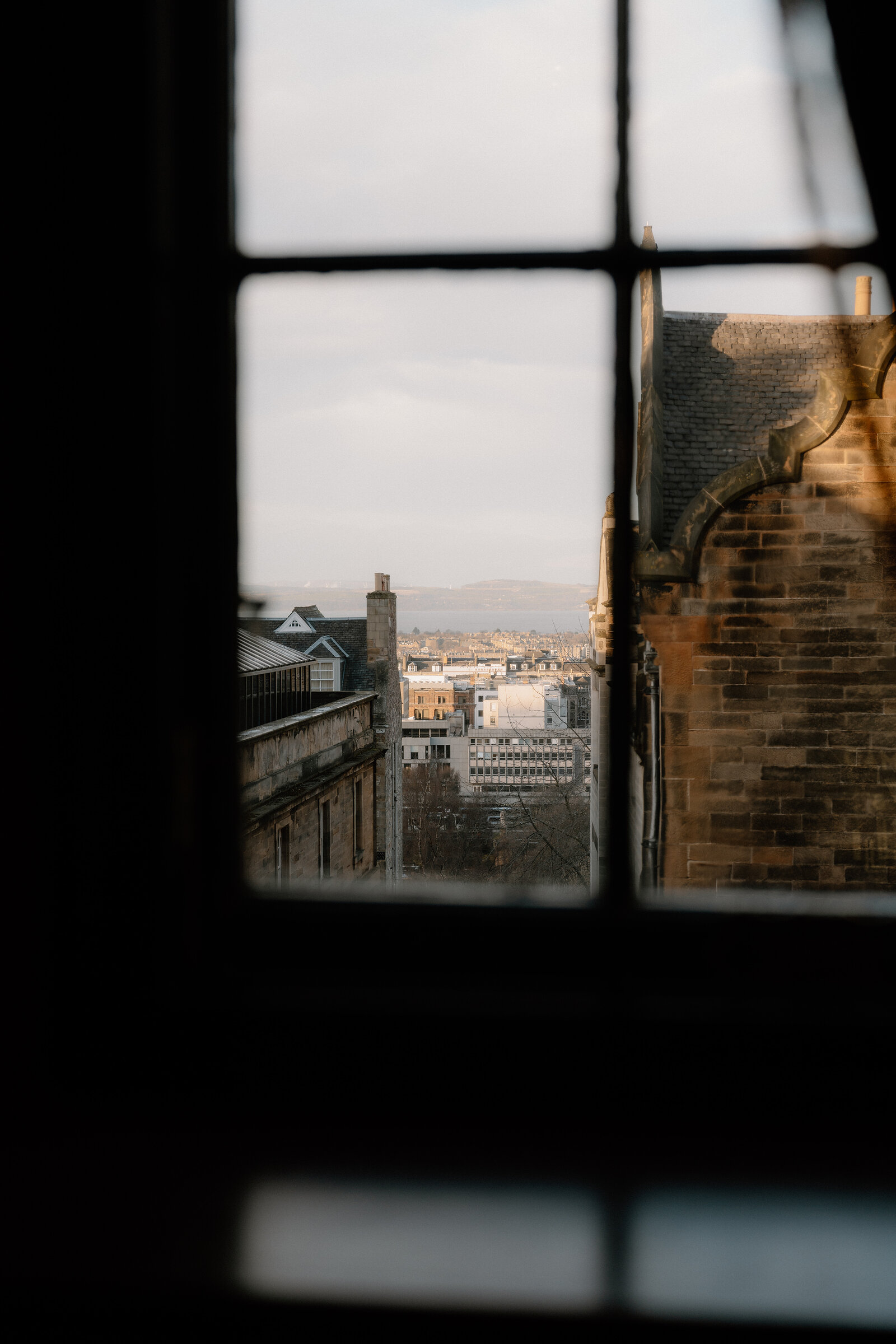 Gothic stone tracery frames a view of Edinburgh's rooftops through a window.