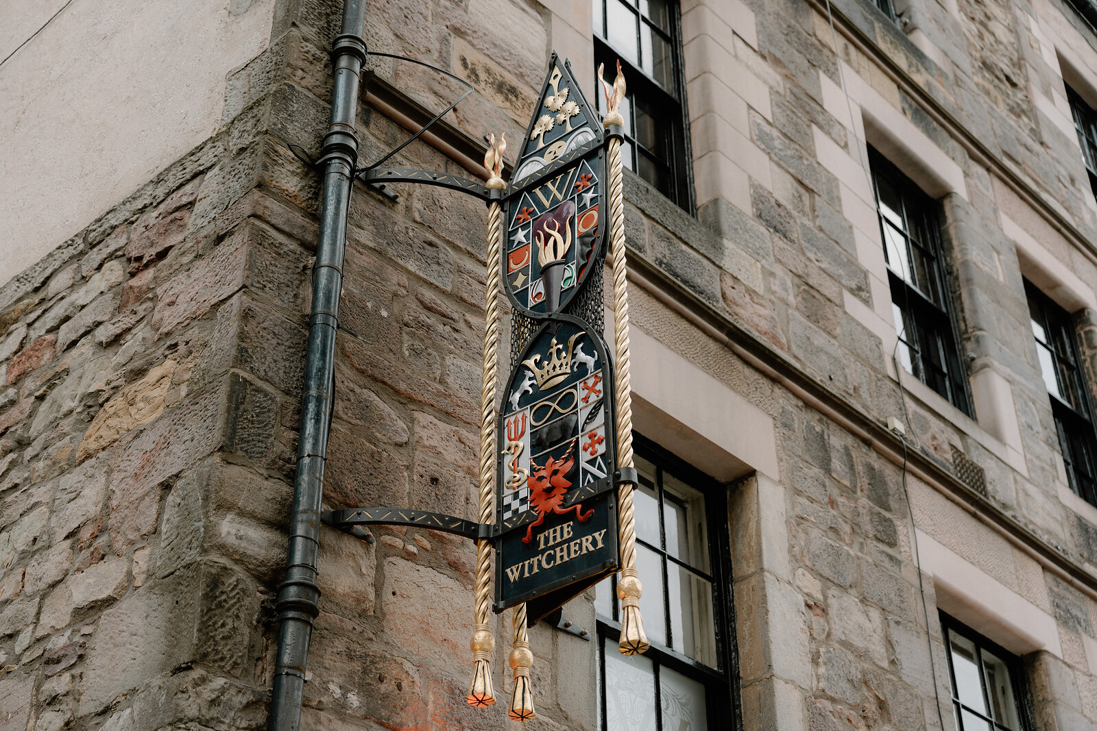 An ornate hanging sign reading 'The Witchery' hangs against a sandstone building.