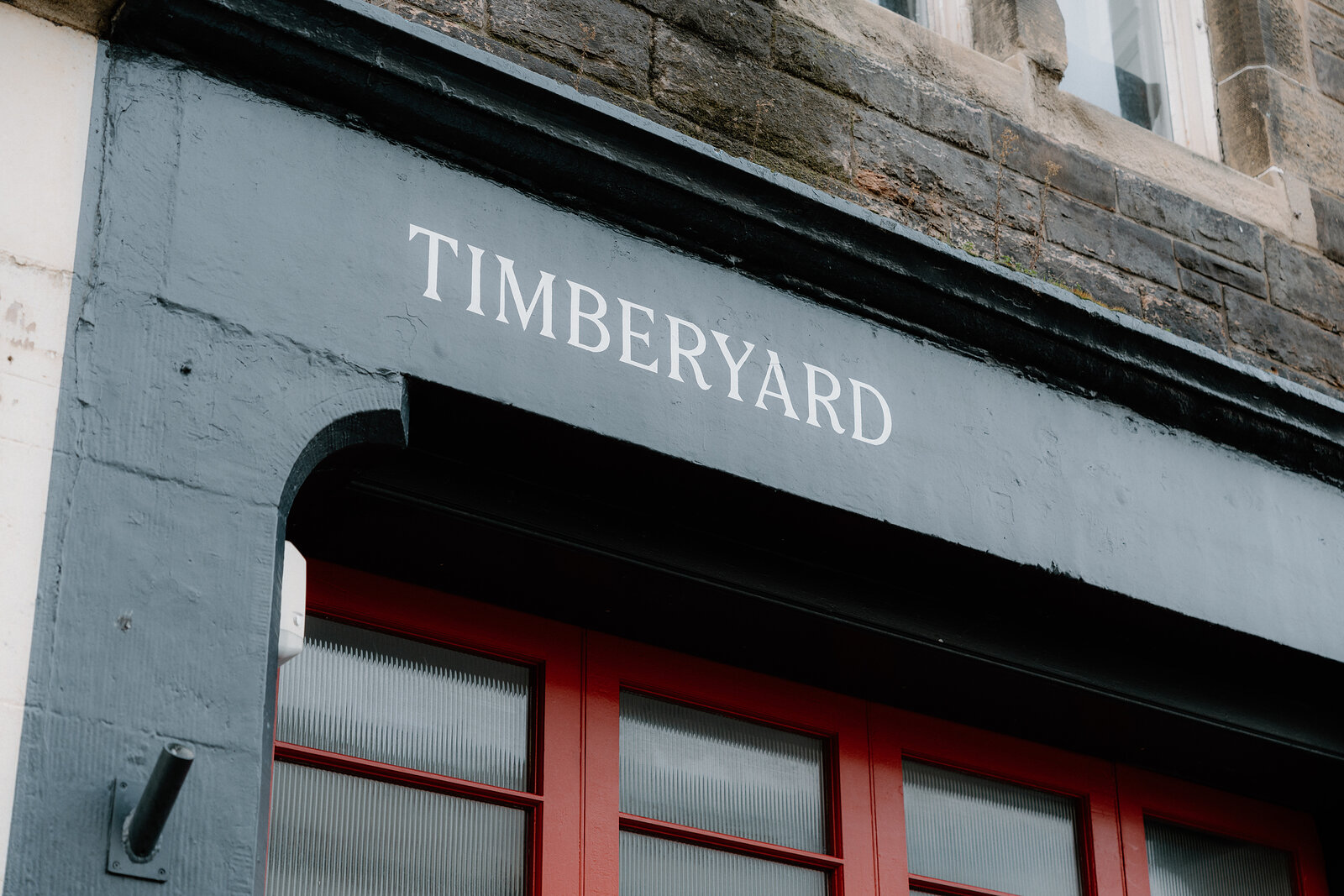 White lettering reading Timberyard spans a dark grey fascia above red-framed windows.