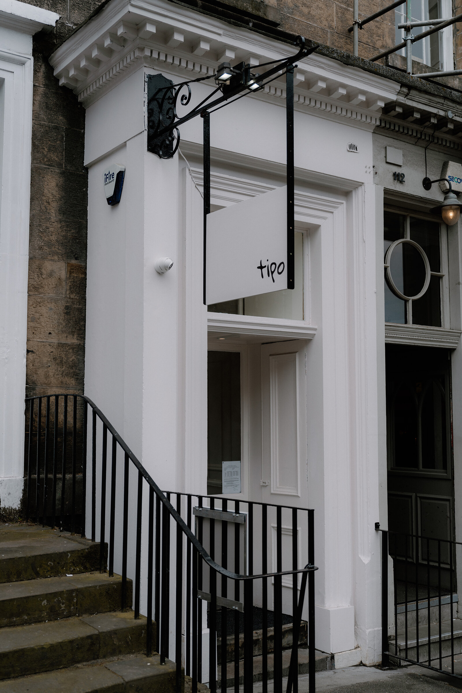 The tipo sign hangs above the entrance of a white Georgian townhouse, reached by a short flight of stone steps and black railings.