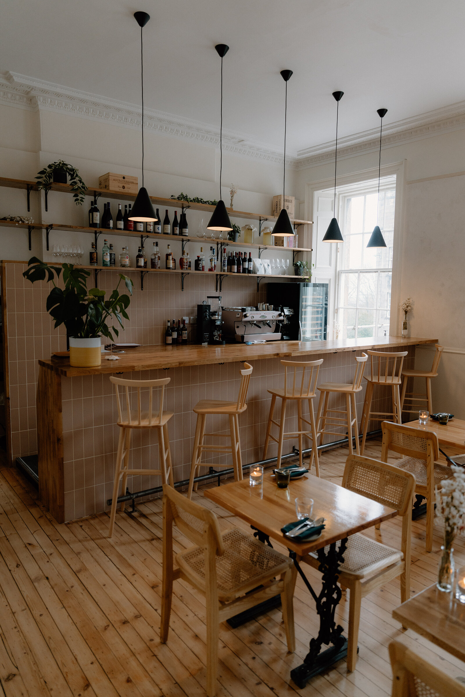 Wooden bar stools line the tiled counter at tipo, its shelves stocked with wine bottles beneath a row of black pendant lights, with tables set nearby.