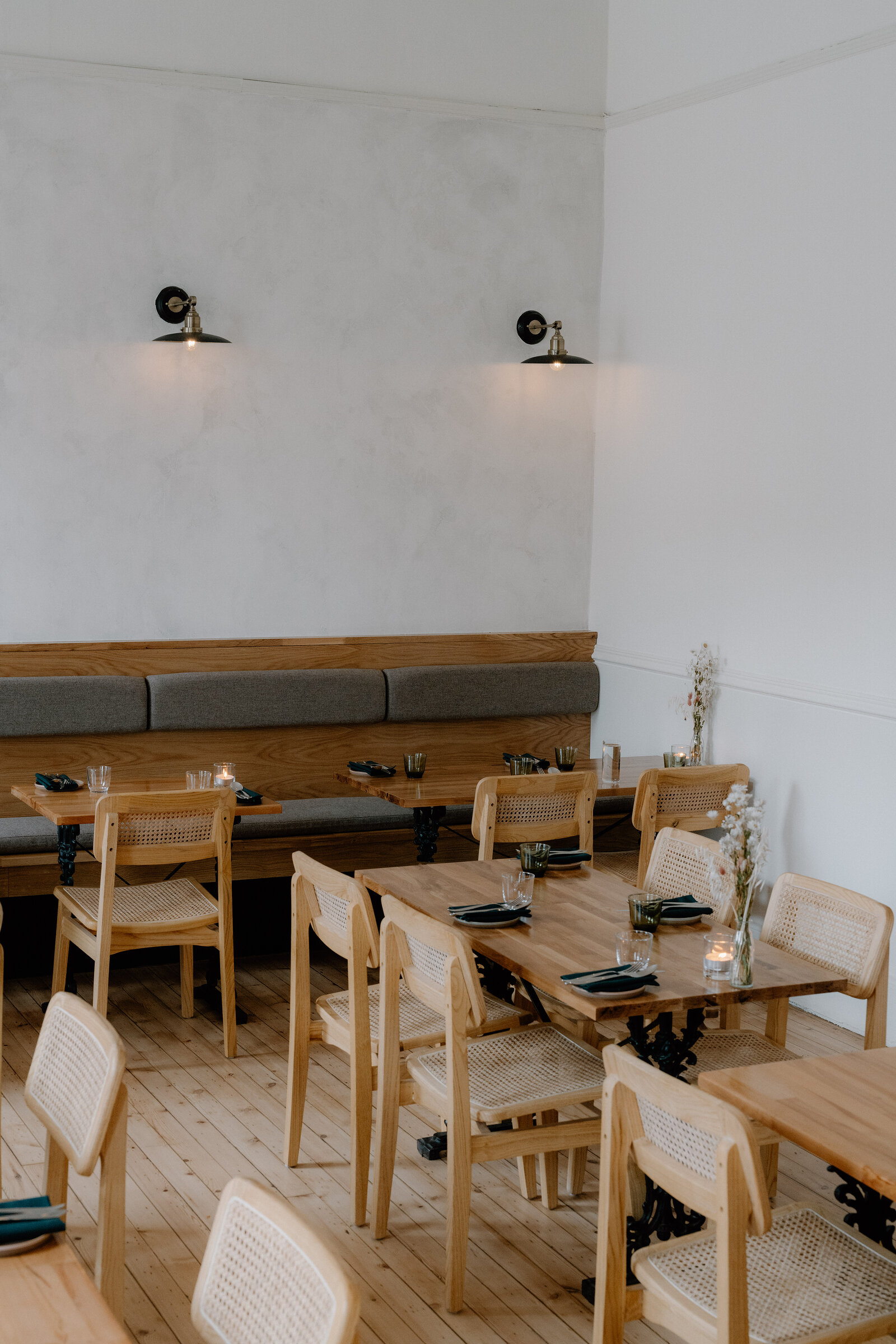 Cane-backed chairs surround wooden tables set with candles and glassware beneath a banquette and wall lamps in the tipo dining room.