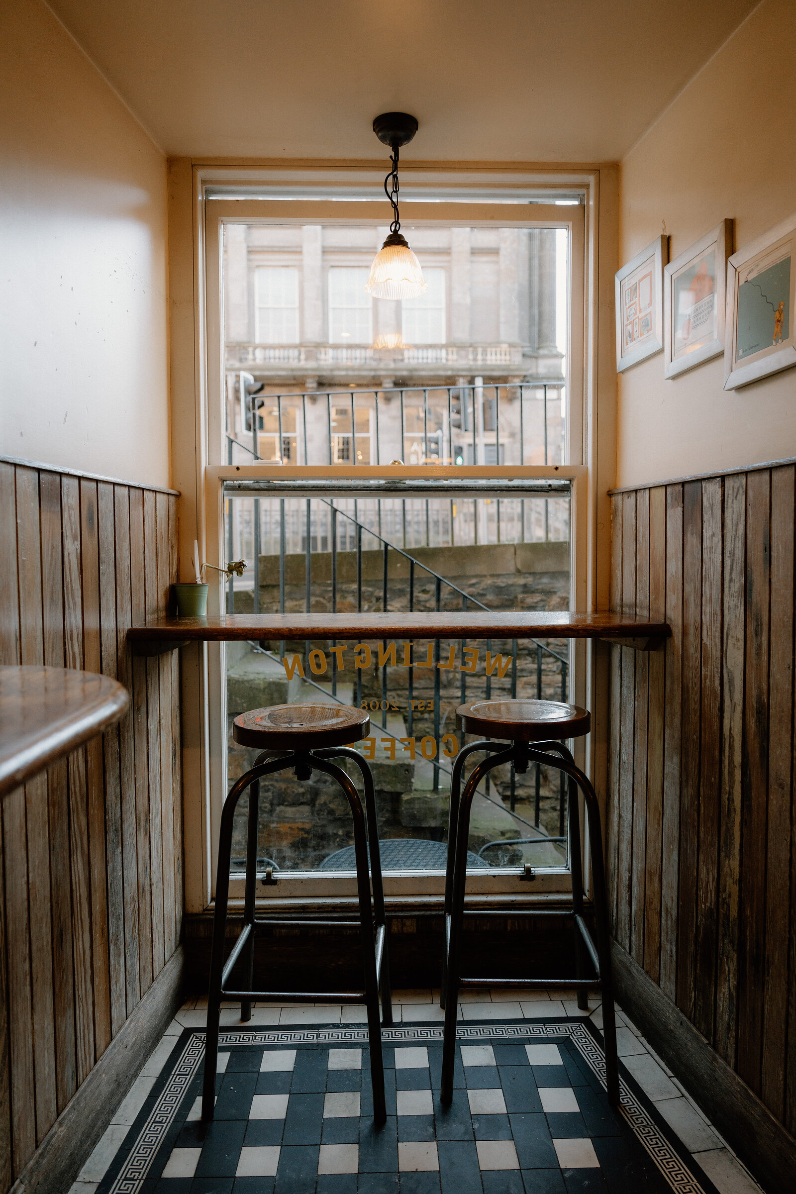 Two stools sit at a narrow window bar etched with Wellington Coffee lettering, looking out over a sandstone terrace.