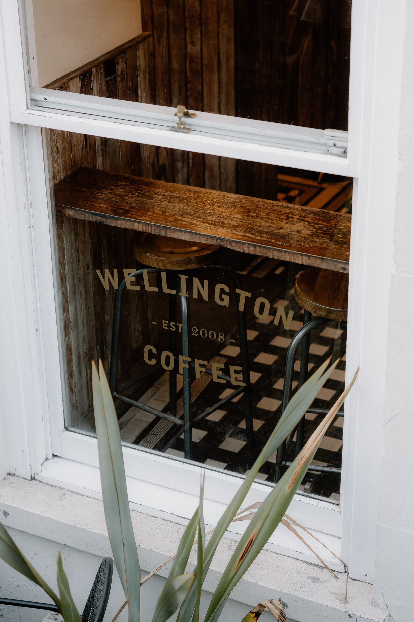 Wellington Coffee, Est 2008, is etched in gold lettering on the cafe's window above a wooden bar and stools inside.