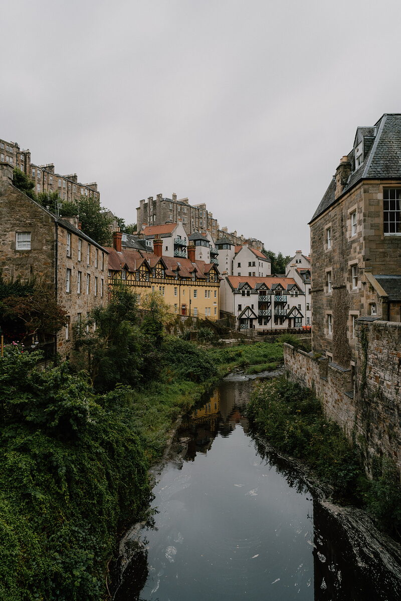 Timber-fronted houses line the Water of Leith at Dean Village, with the Old Town skyline rising behind.