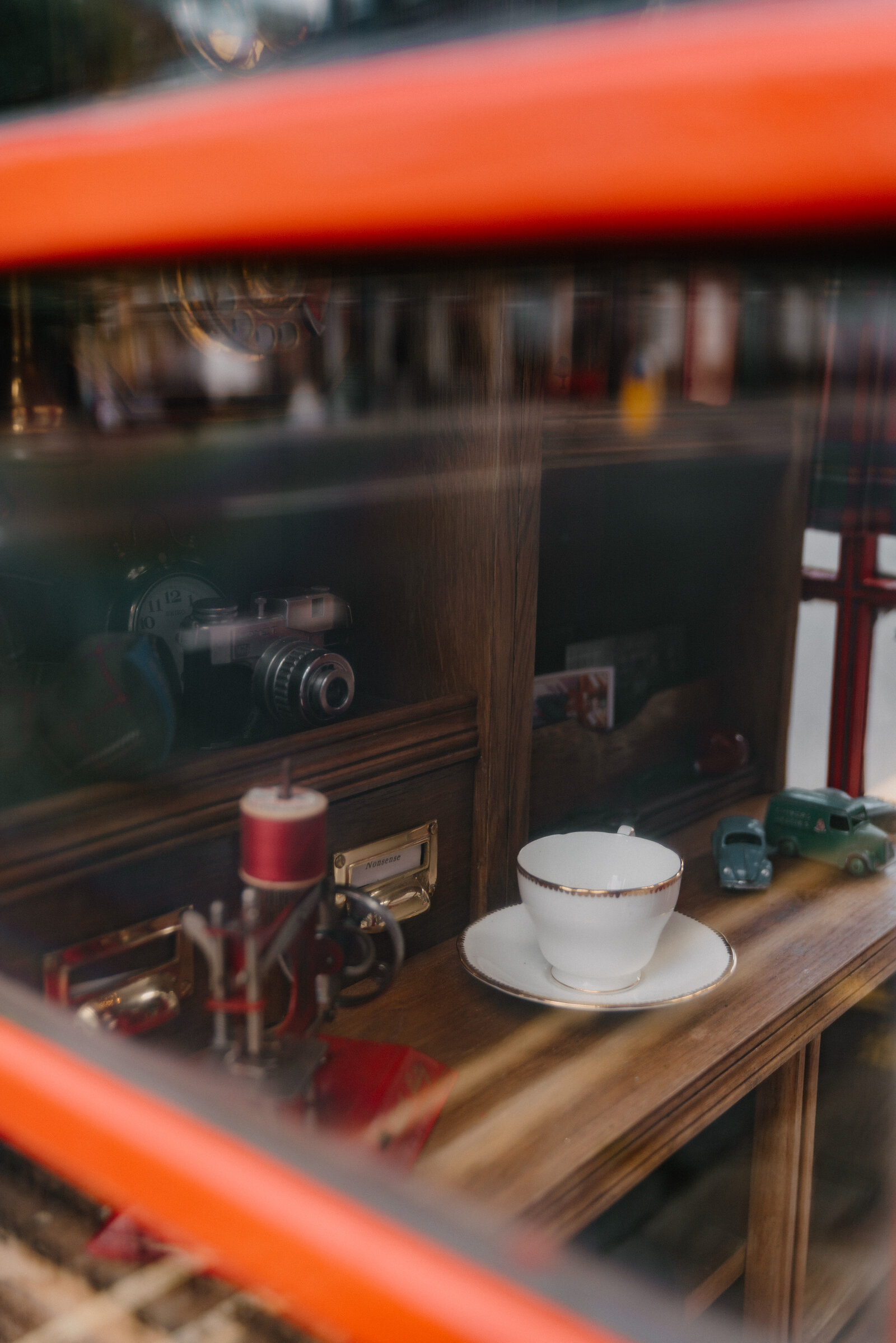A vintage camera, a teacup and saucer, and toy cars are arranged behind the glass of Gilbert the phone box