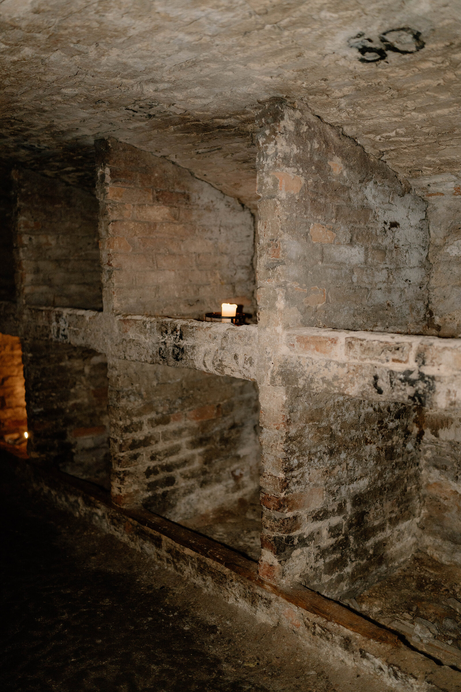 Brick-vaulted alcoves underground, a single candle lit on a ledge