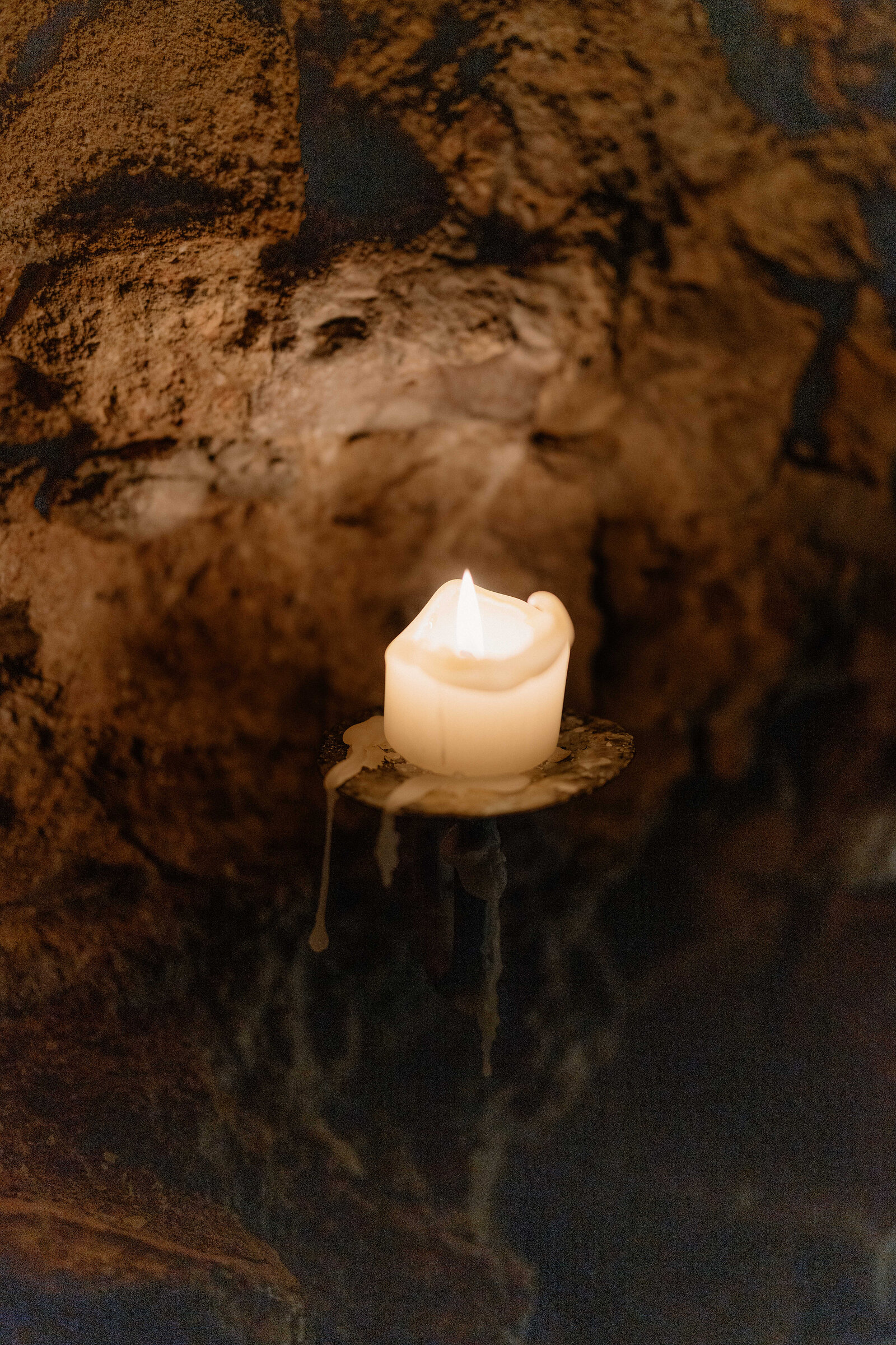 A single candle lit against a rough rock wall underground