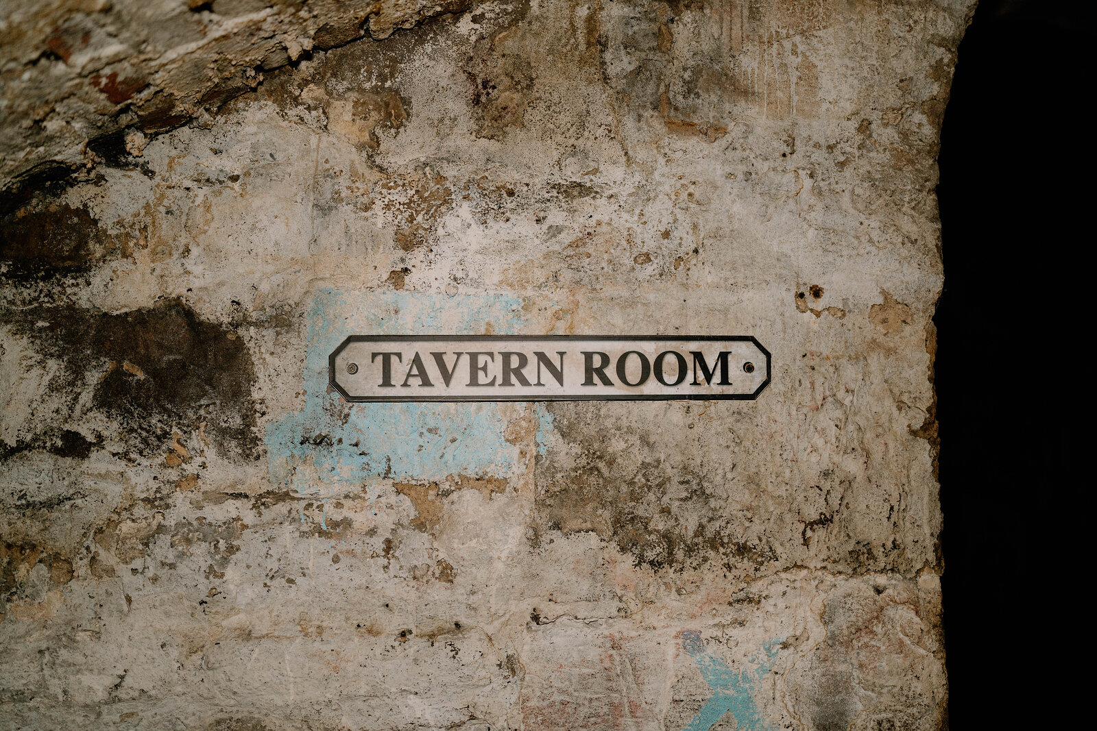 A "Tavern Room" sign mounted on a rough stone wall underground