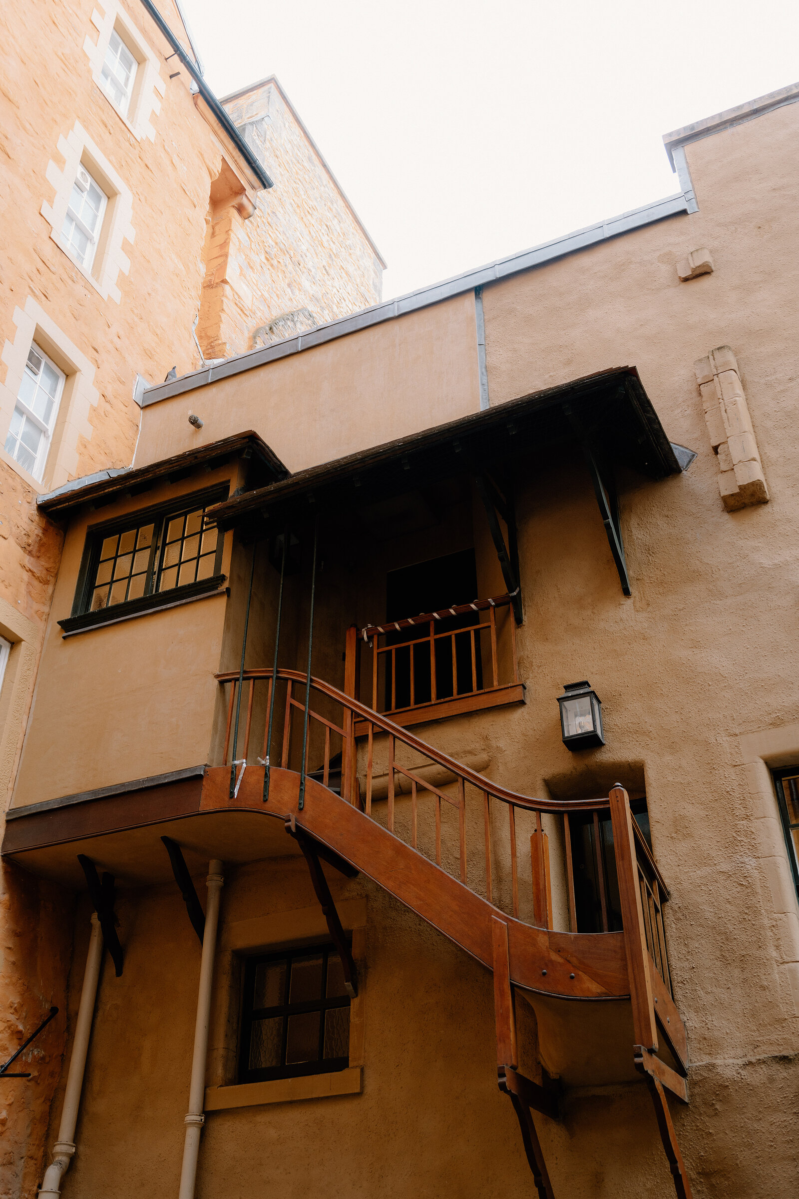 A wooden external staircase climbing the sandstone rear wall of a tenement