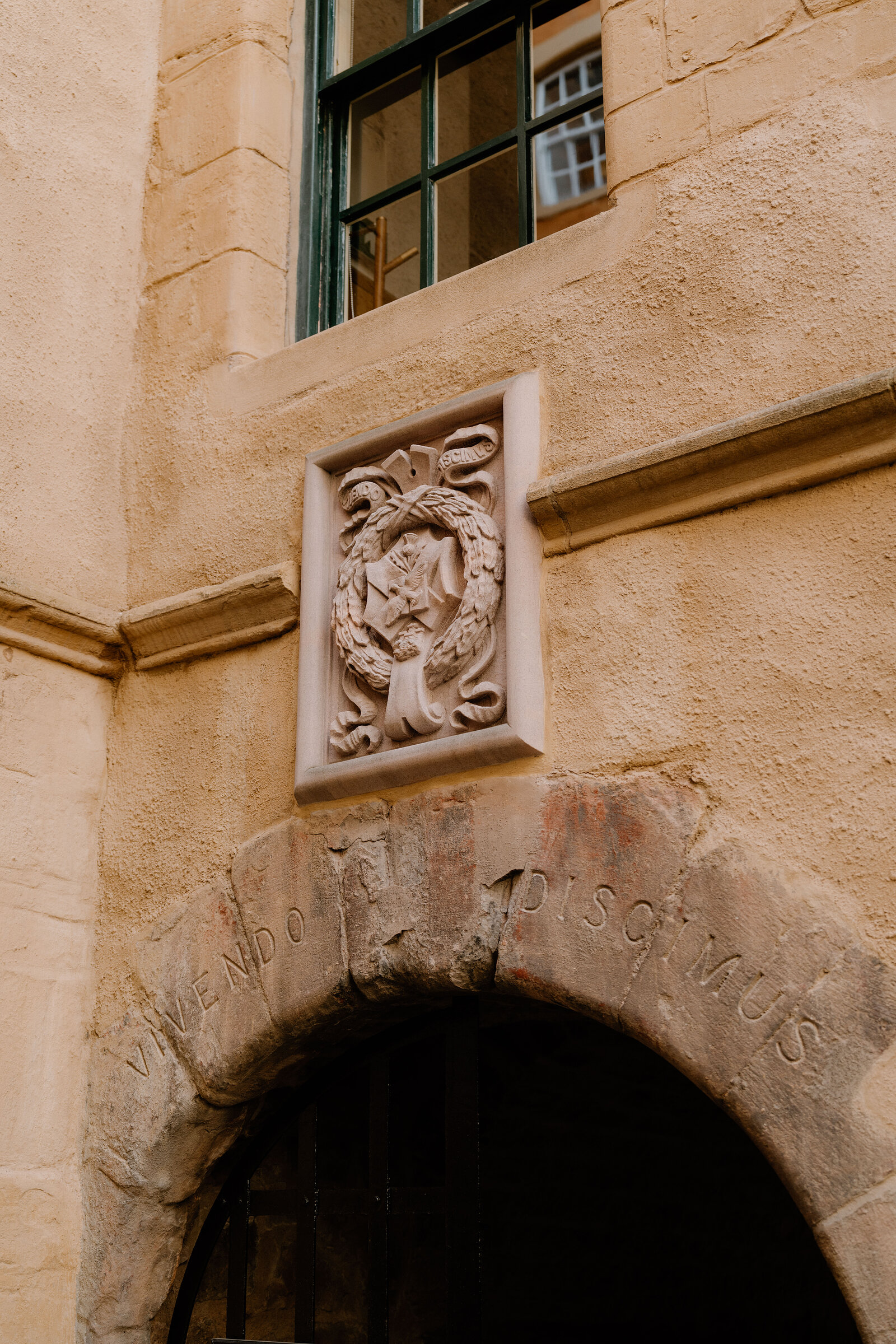 A carved crest above an archway inscribed with the motto Vivendo Discimus
