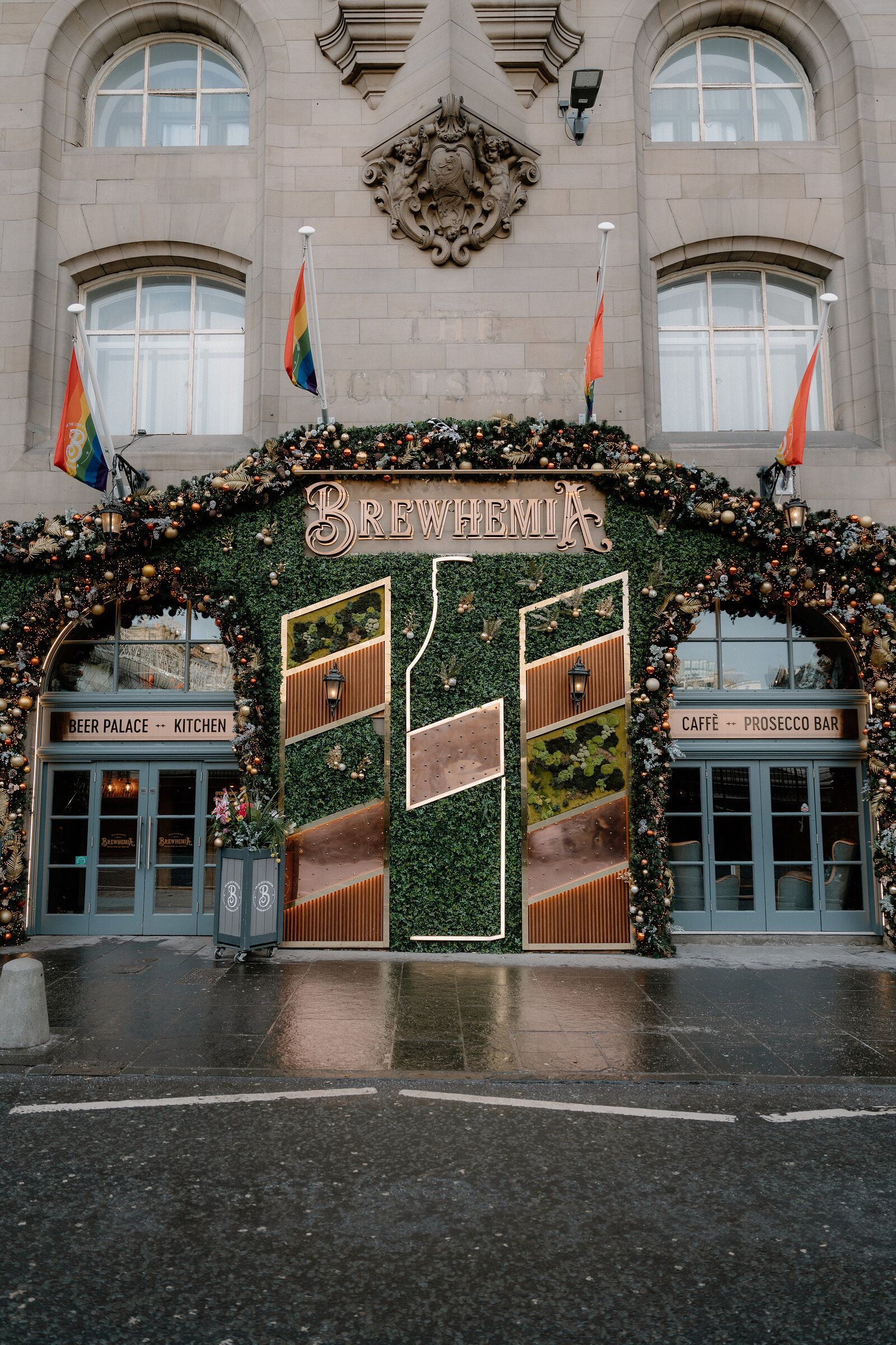 The carved crest above Brewhemia's greenery-clad entrance, rainbow flags flying either side