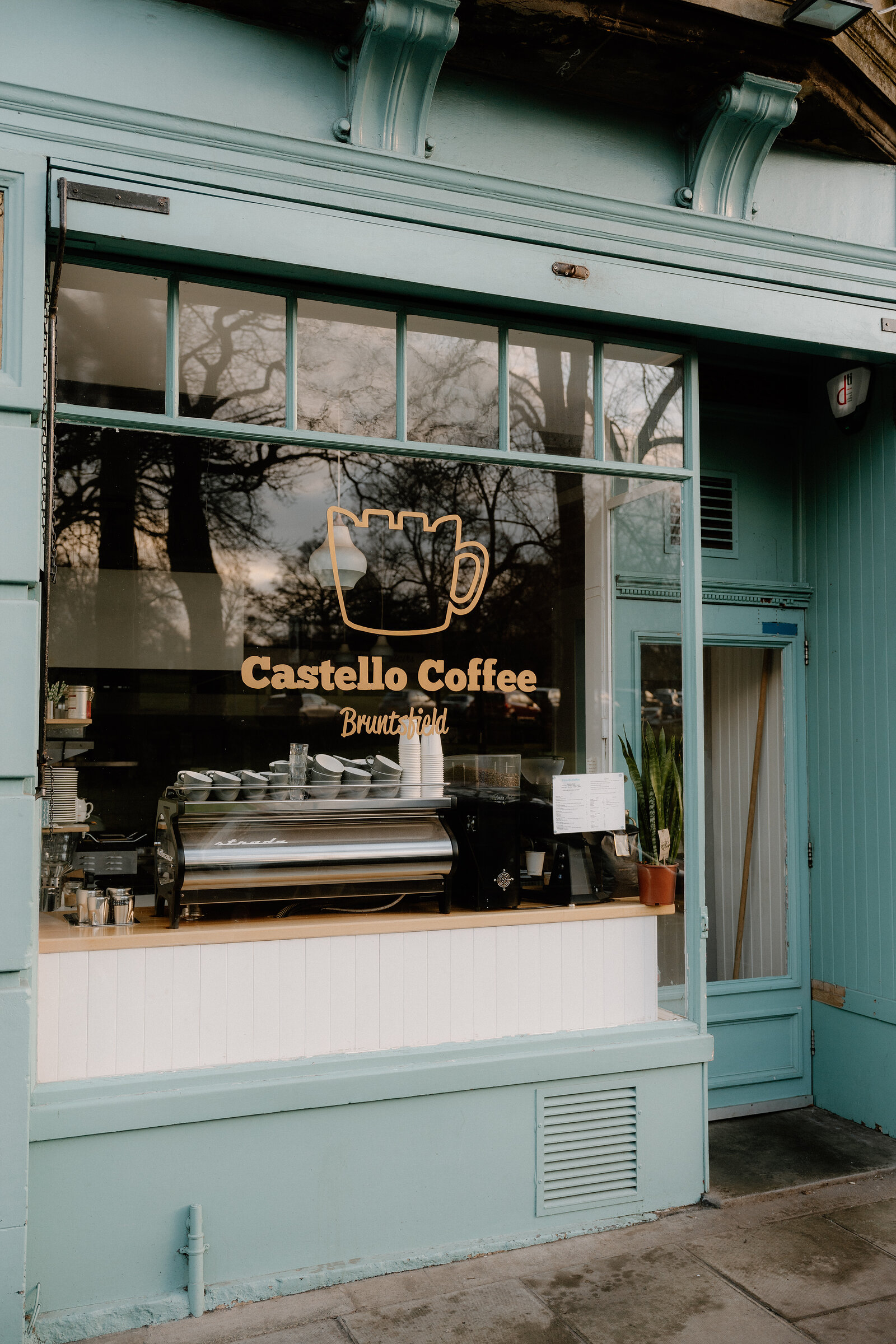 The pale green shopfront of Castello Coffee, its espresso machine visible through the window