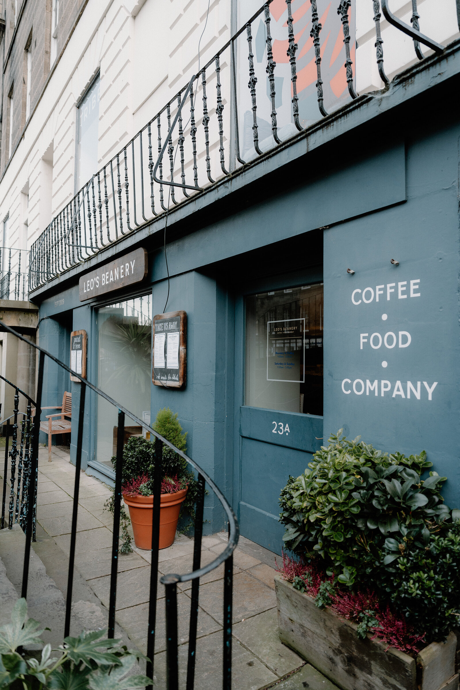 Leo's Beanery's blue frontage beneath its Coffee Food Company signage, potted plants lining the pavement.