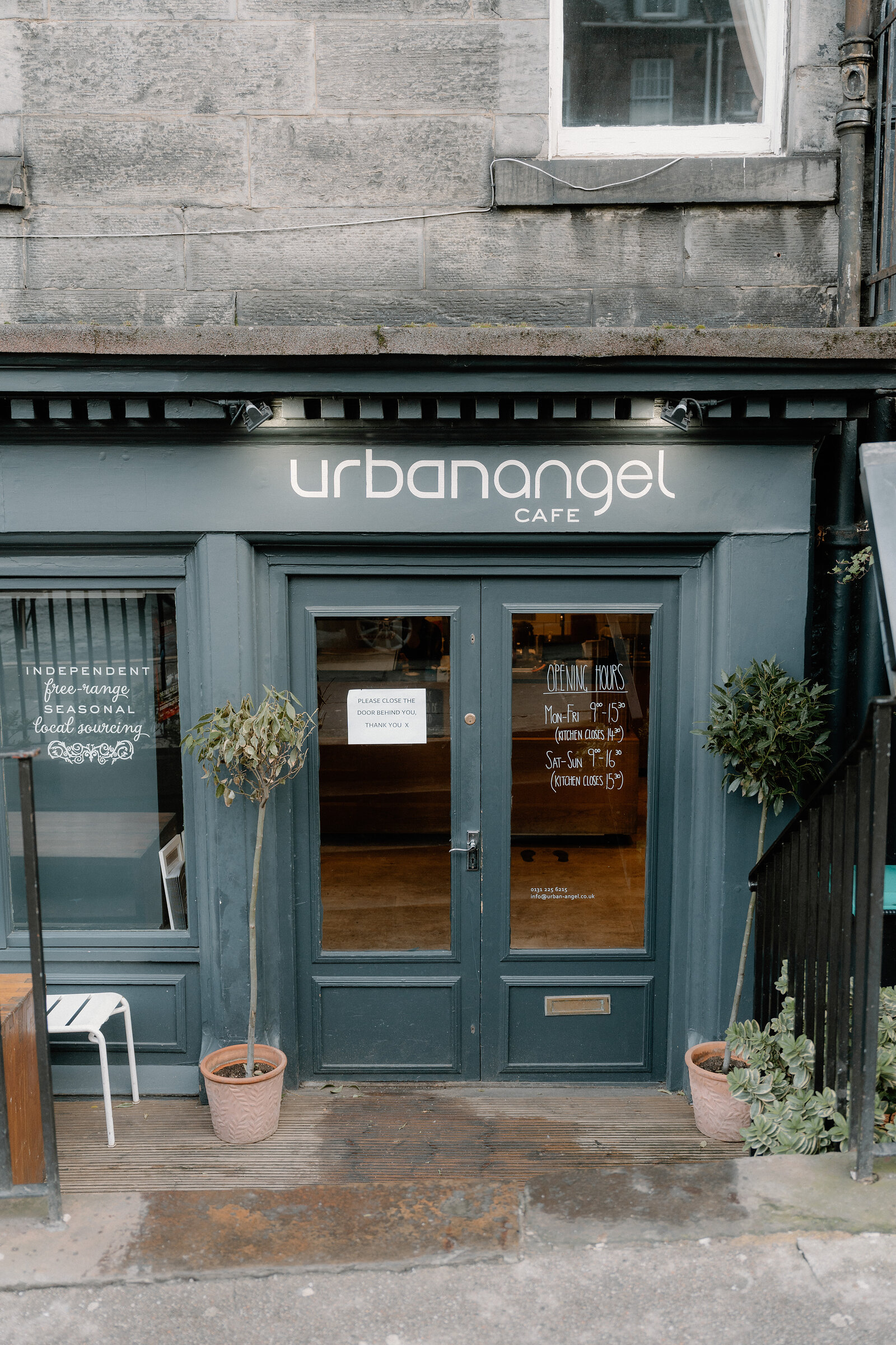 The teal shopfront of Urban Angel Cafe, potted topiaries flanking its double doors