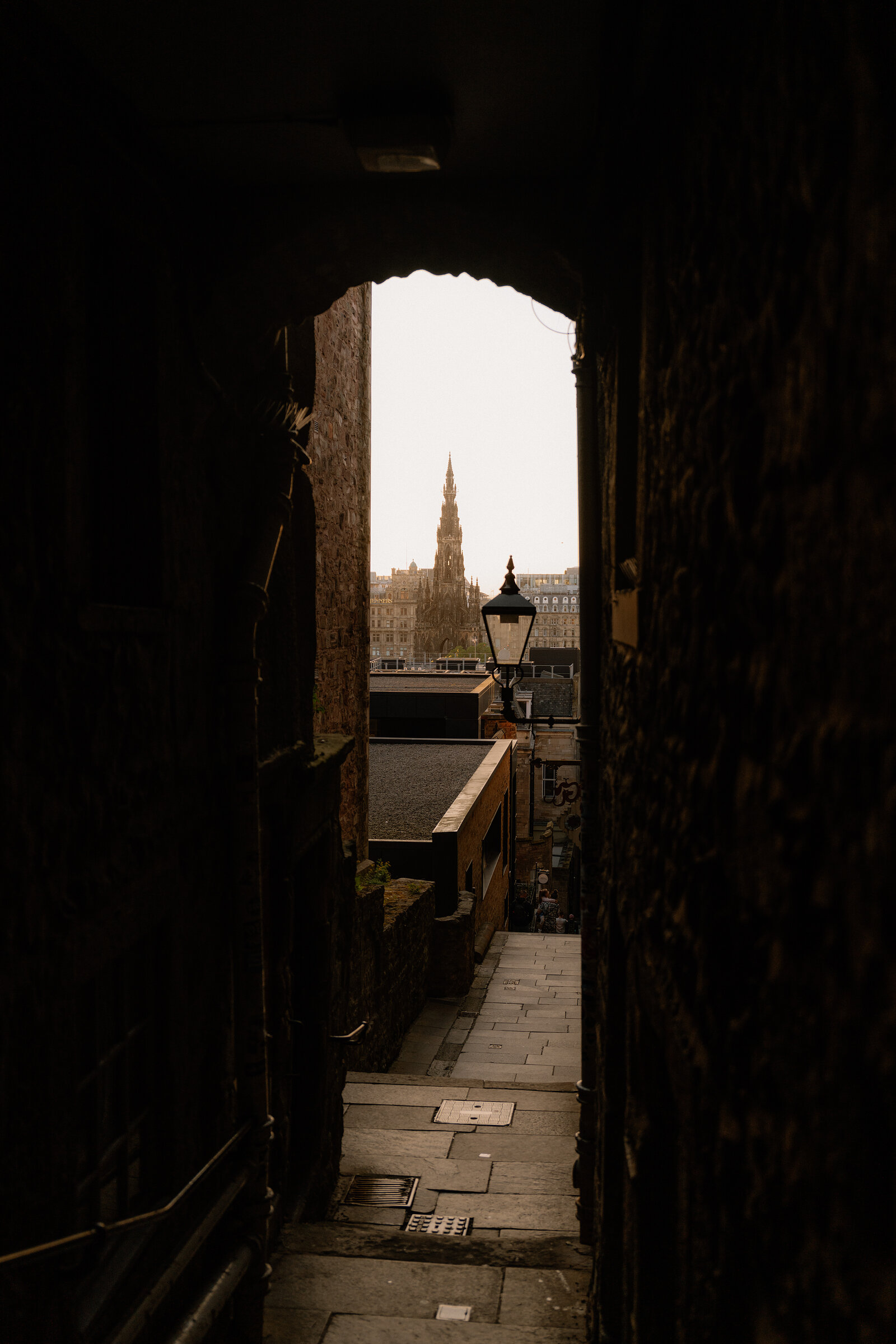 A narrow close framing a distant spire, a lamppost standing at the foot of the steps beyond the archway.