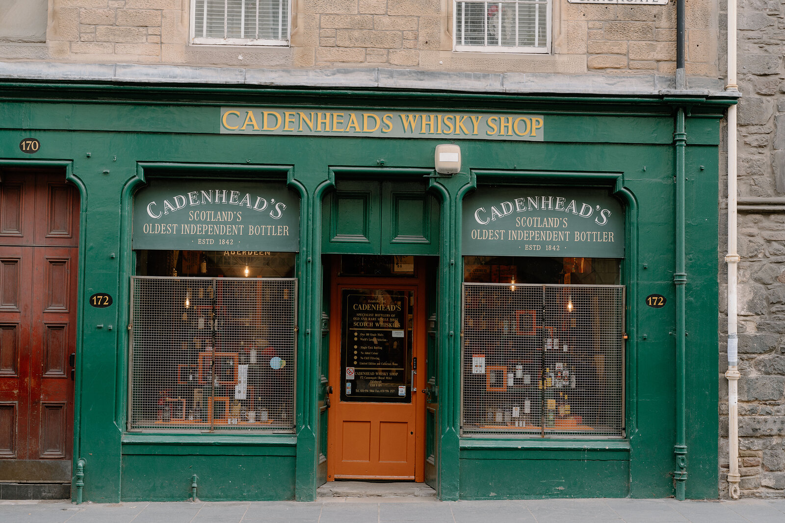 Cadenhead's Whisky Shop has a green-painted Edinburgh shopfront with gold lettering reading 'Scotland's Oldest Independent Bottler' above bottle-filled windows.