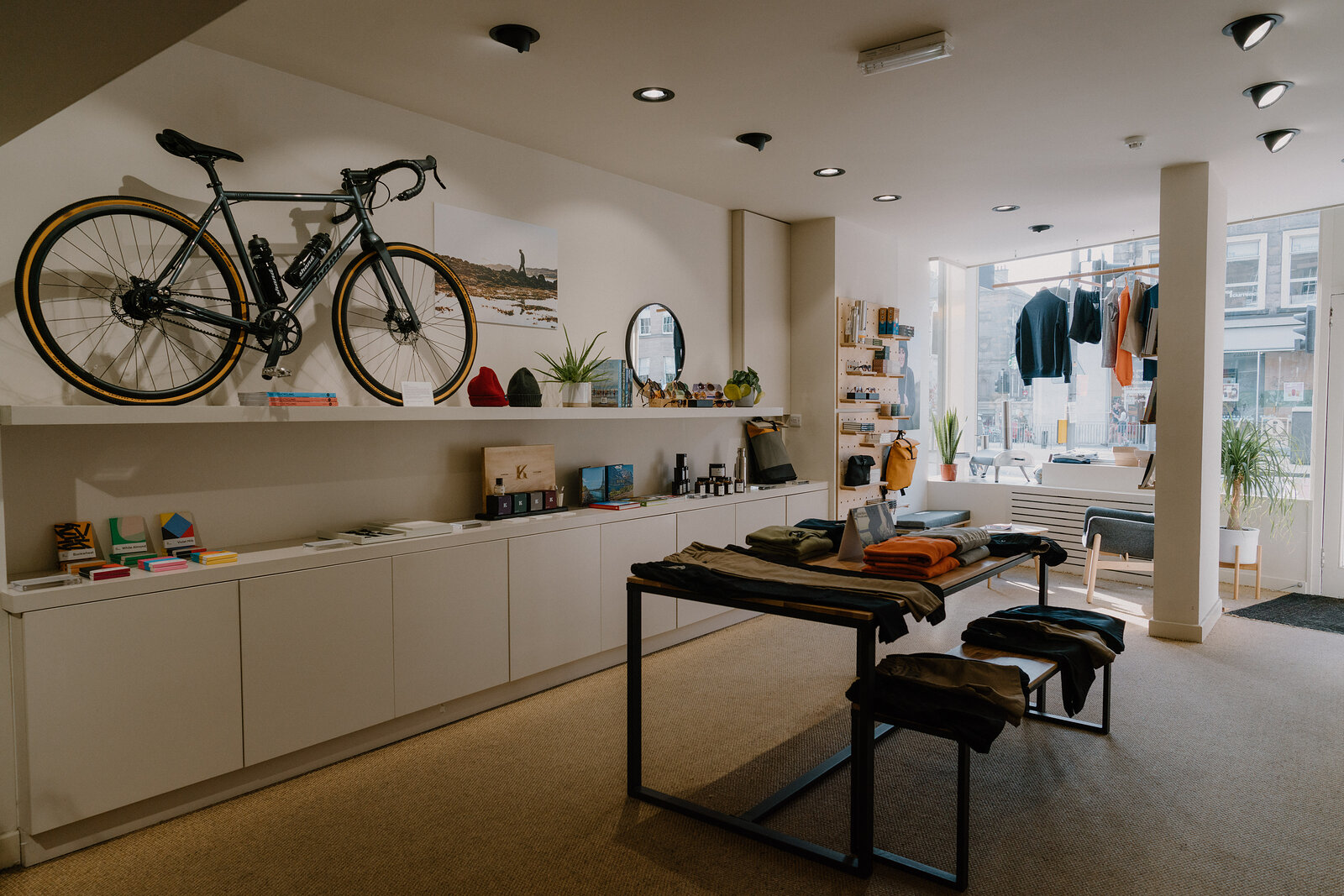 A road bicycle mounted on the wall above a low cabinet display in a clothing shop