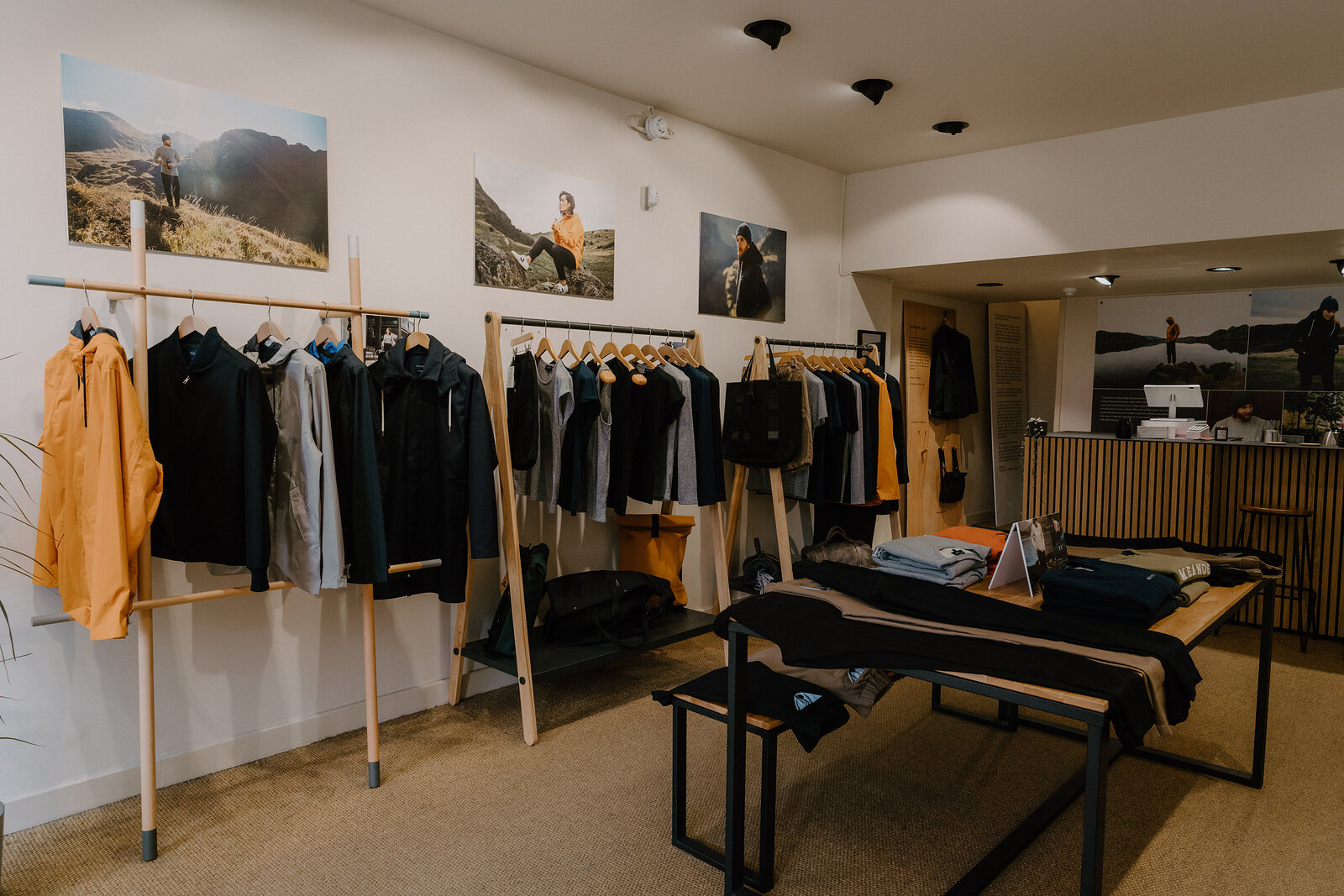 Clothing rails beneath mountain photographs in a shop, a table of folded garments in the foreground