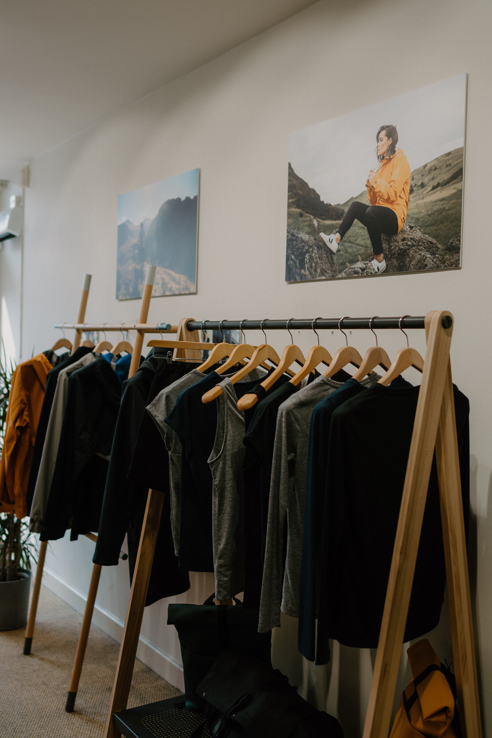 A clothing rail of jumpers and jackets beneath mountain photography prints on a shop wall