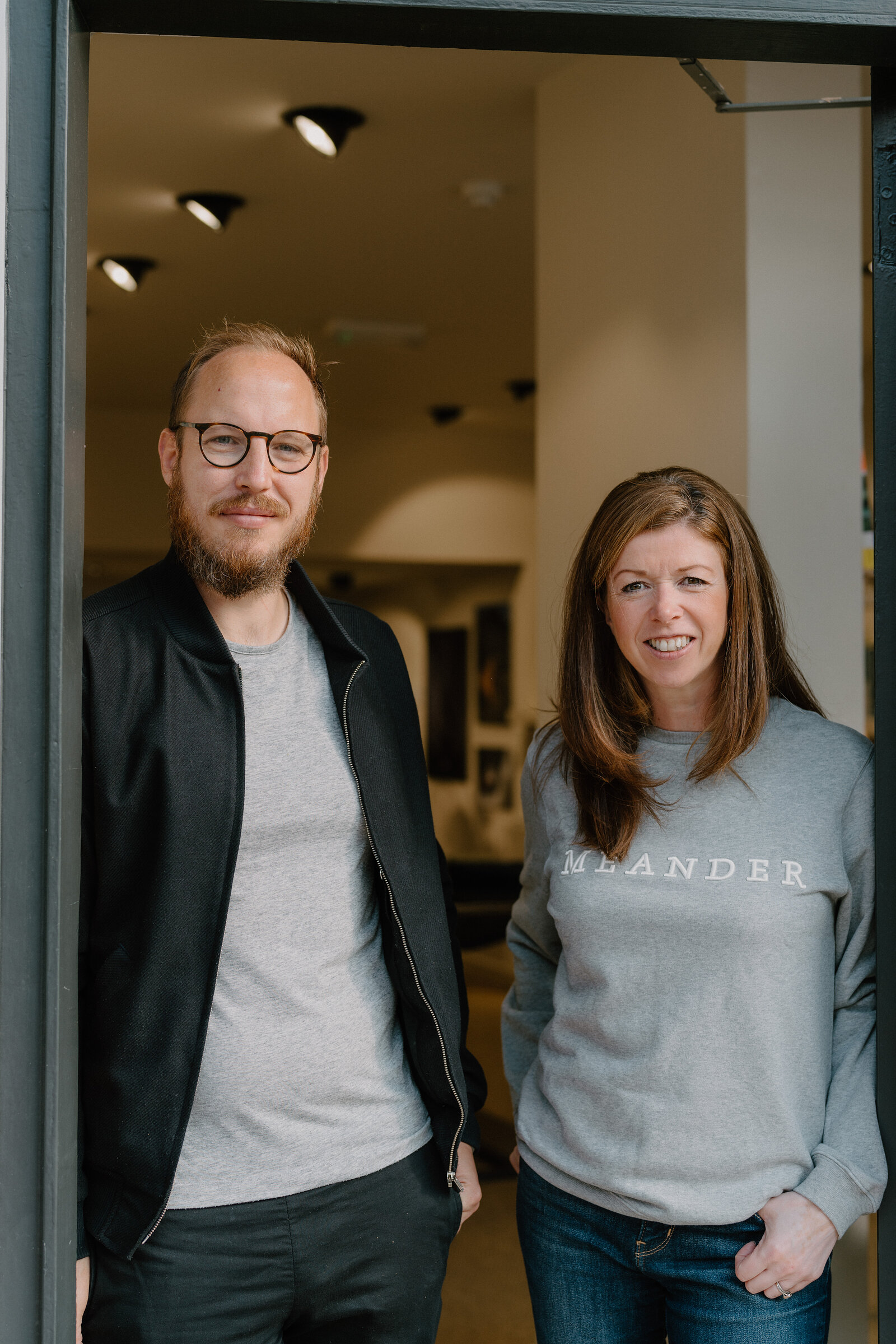 A man and a woman in a branded Meander sweatshirt standing together in a shop doorway