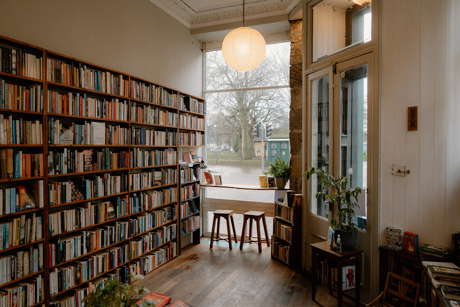 A reading nook at the end of a book-lined room, stools set by a bright window overlooking a park