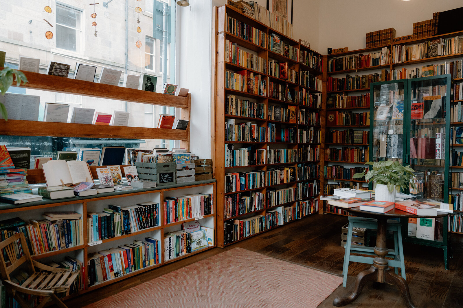 A book-lined room with a tiered display table beneath a tall window, shelves reaching to the ceiling