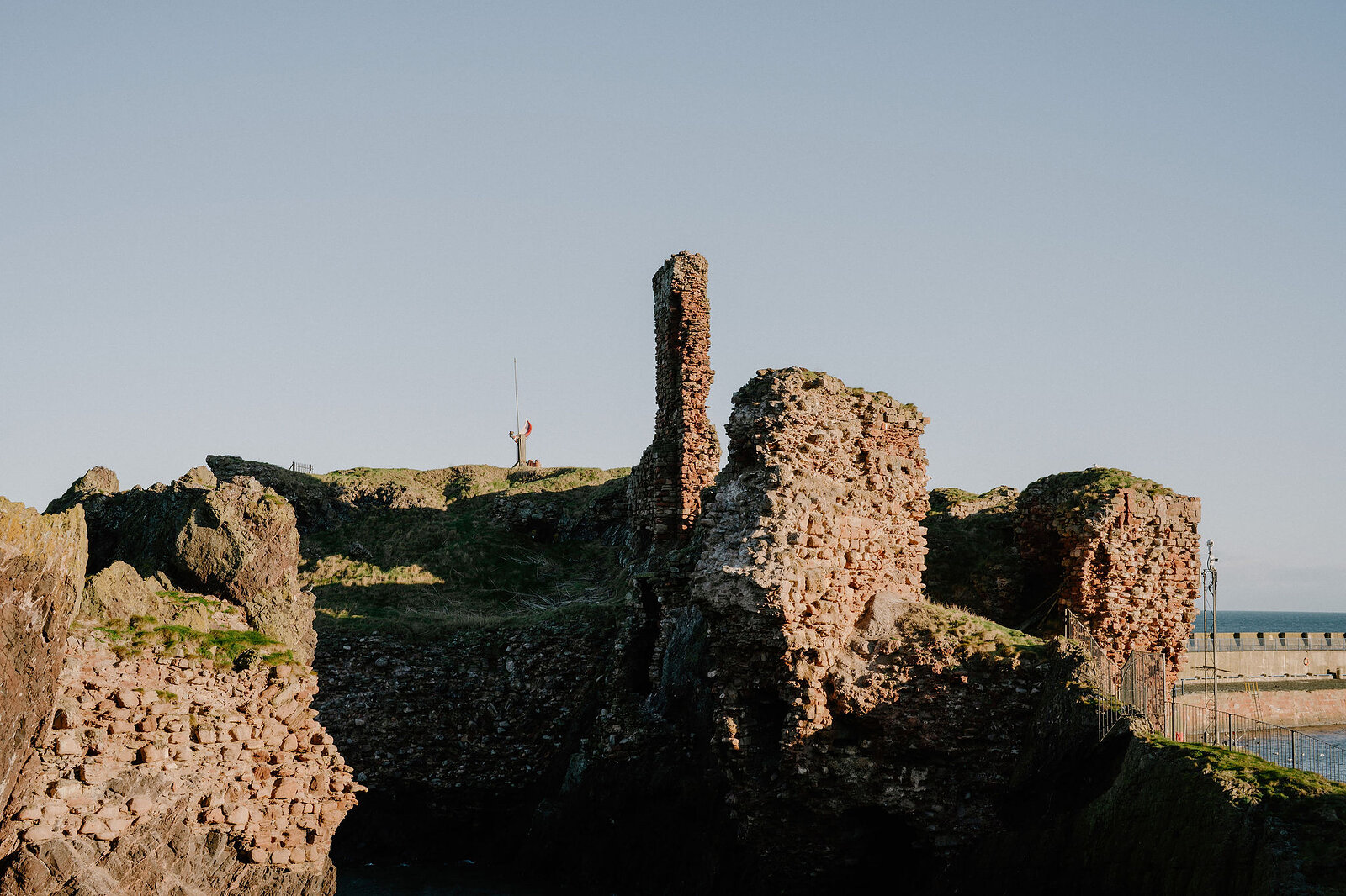 A rocky coastal cove opens beside crumbling stone ruins on the clifftop.