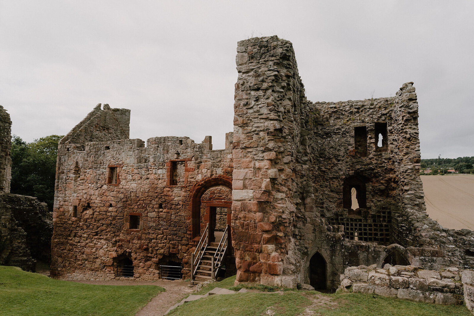 Tantallon Castle's red sandstone gatehouse and tower rise above a wooden bridge and fields beyond.