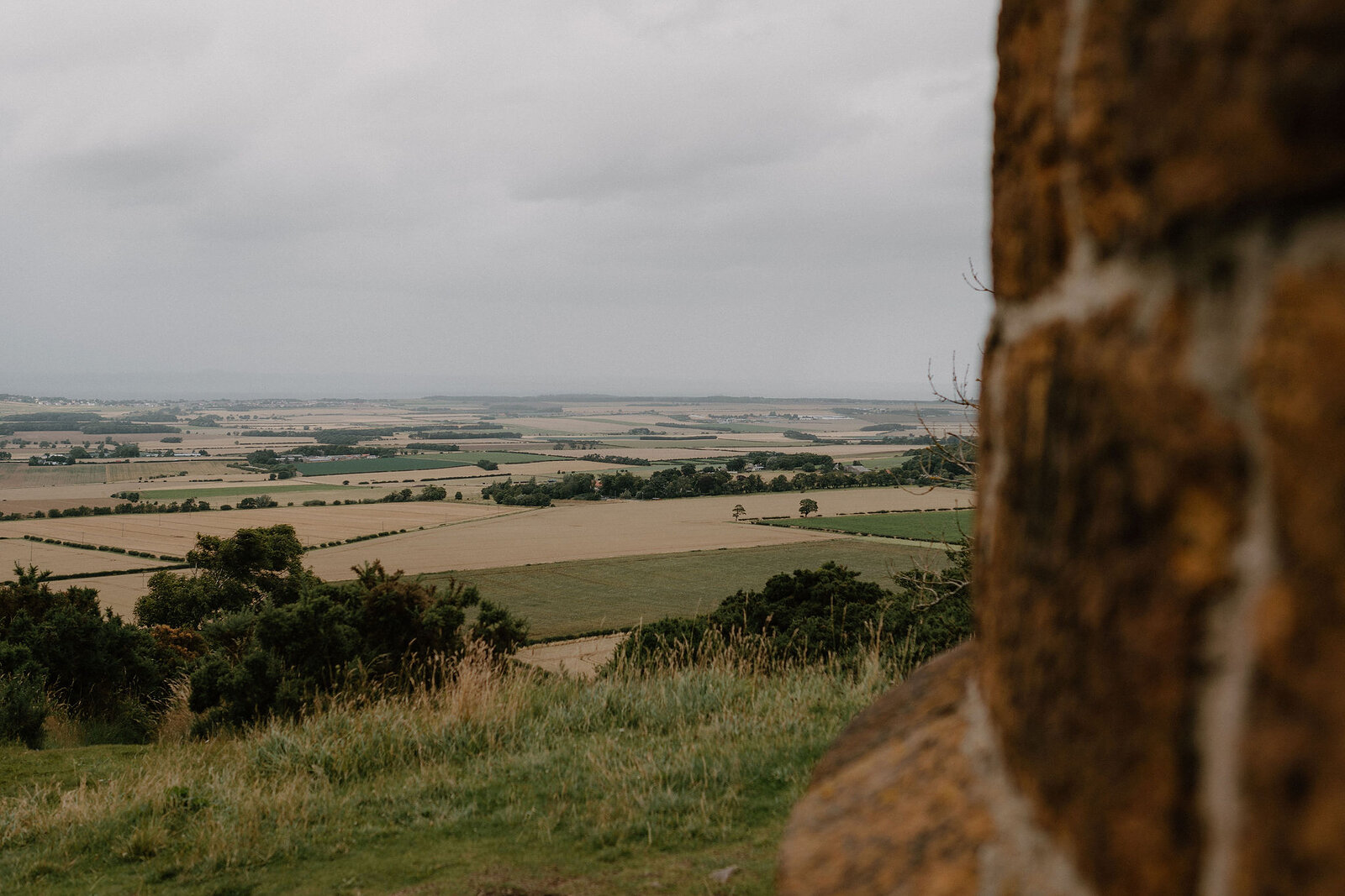 Patchwork fields stretch toward the horizon, seen from a hilltop tower.