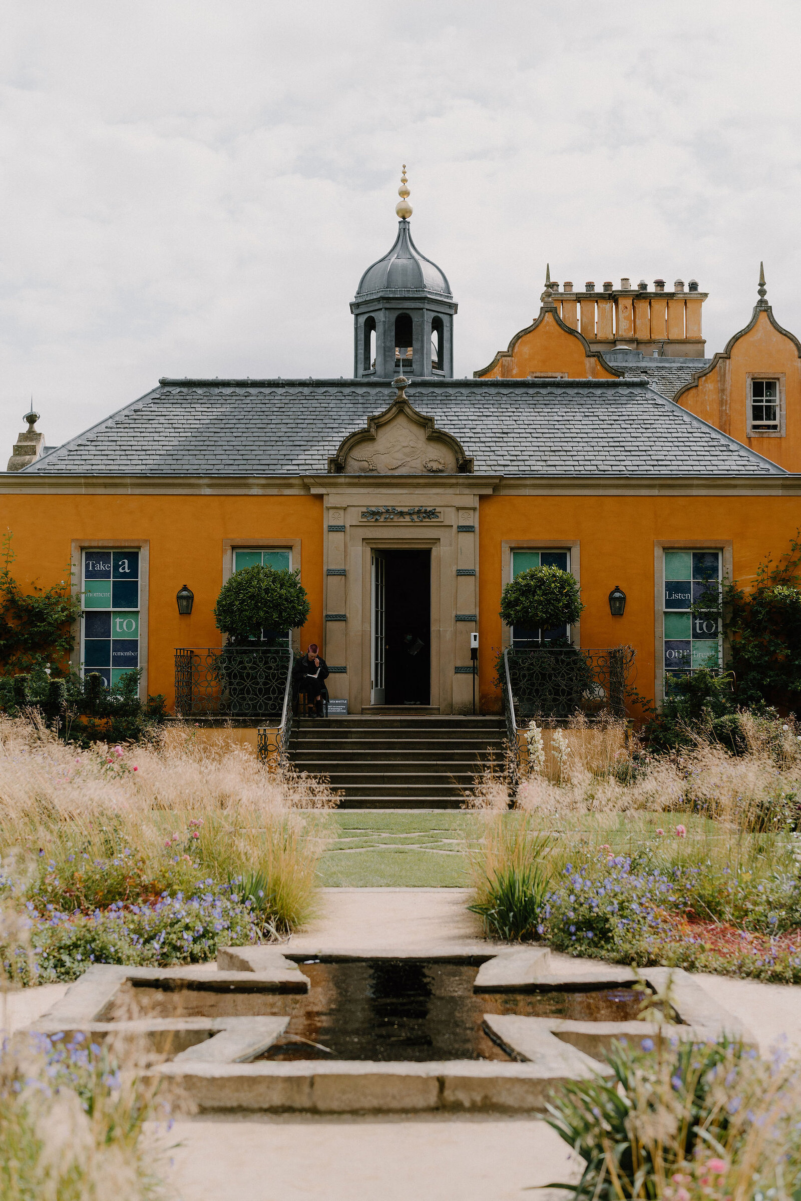 An ochre mansion with a domed cupola overlooks a formal garden and still pool.