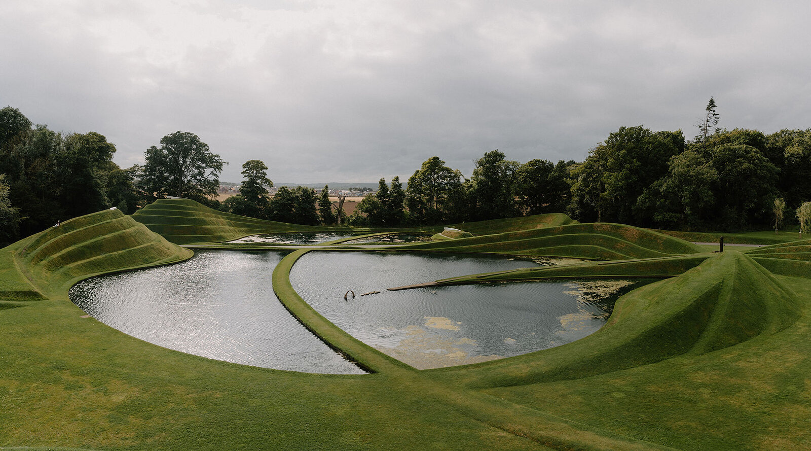 Curving grass mounds ring a still pond in a landscaped garden.