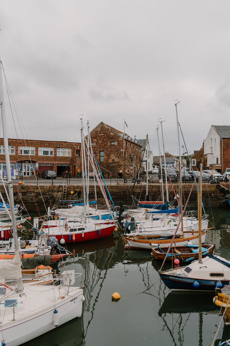 Fishing boats and sailboats crowd a stone harbour before a row of buildings.