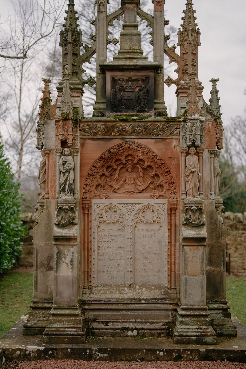 An inscribed panel sits beneath a carved arch on an ornate gothic memorial.