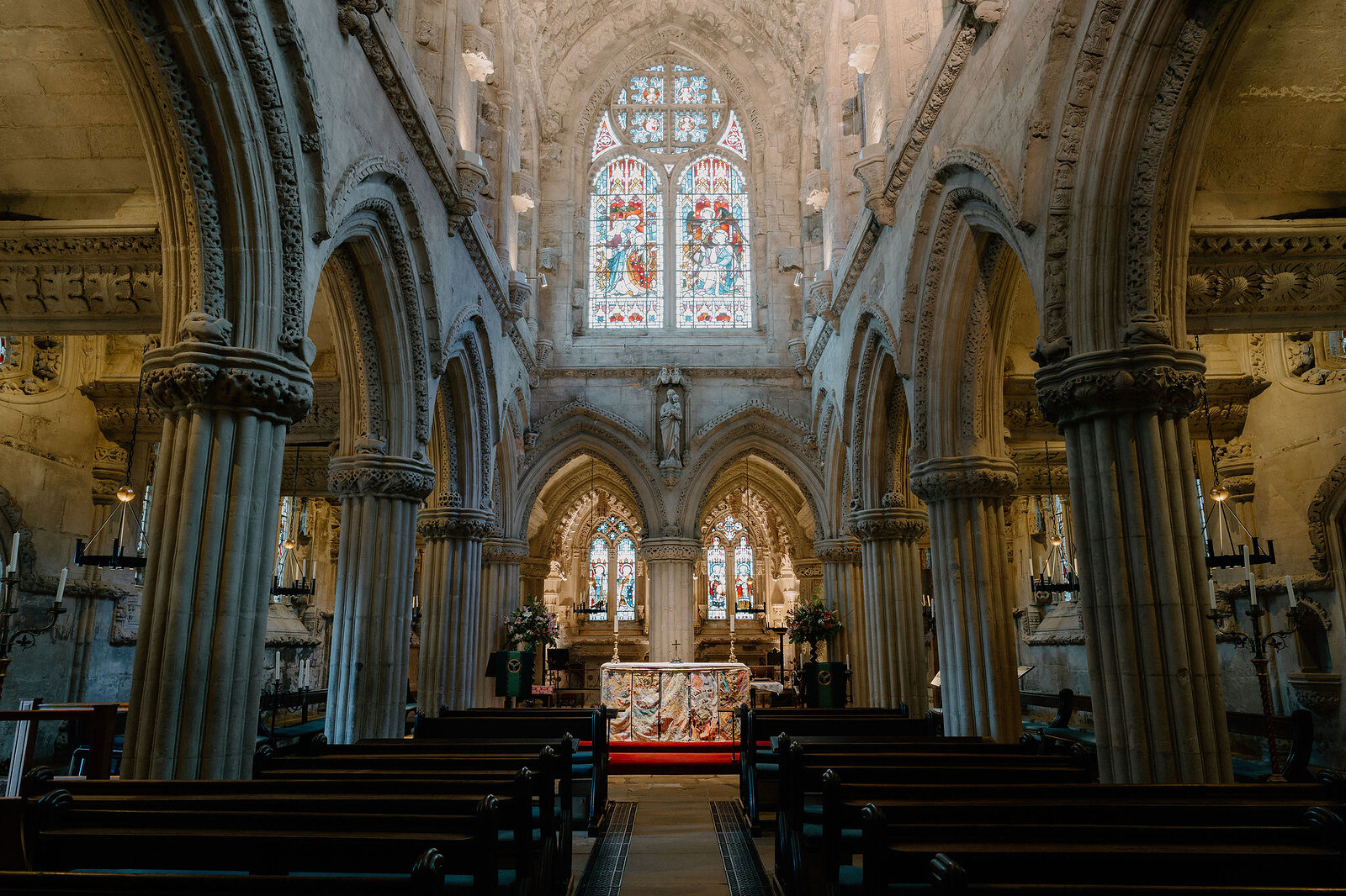 Carved pillars line the nave toward Rosslyn Chapel's stained-glass altar window.