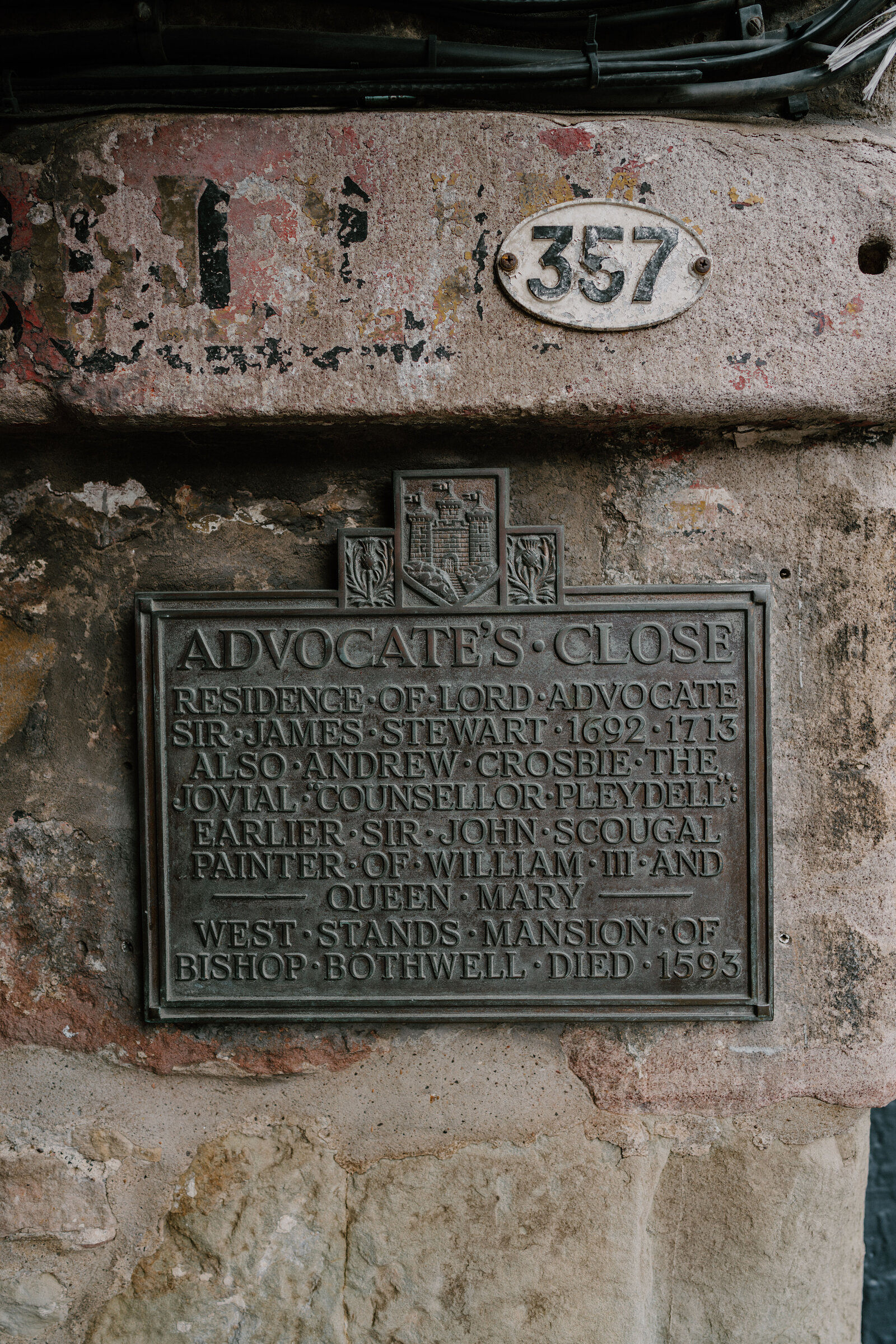 A weathered plaque for Advocate's Close listing its historic residents, mounted beside a numbered oval sign