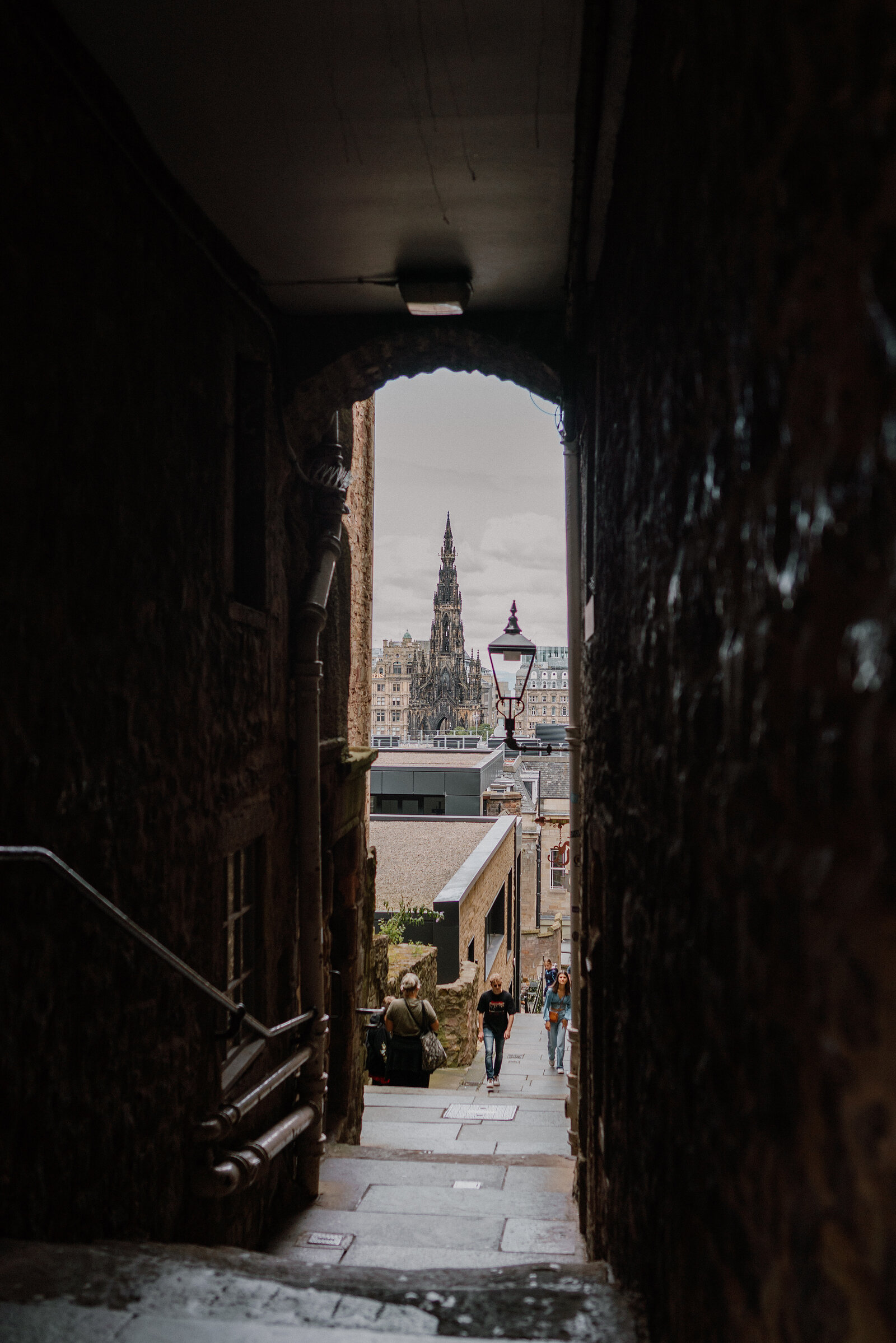 An archway framing a view down a close towards the Scott Monument, pedestrians walking below