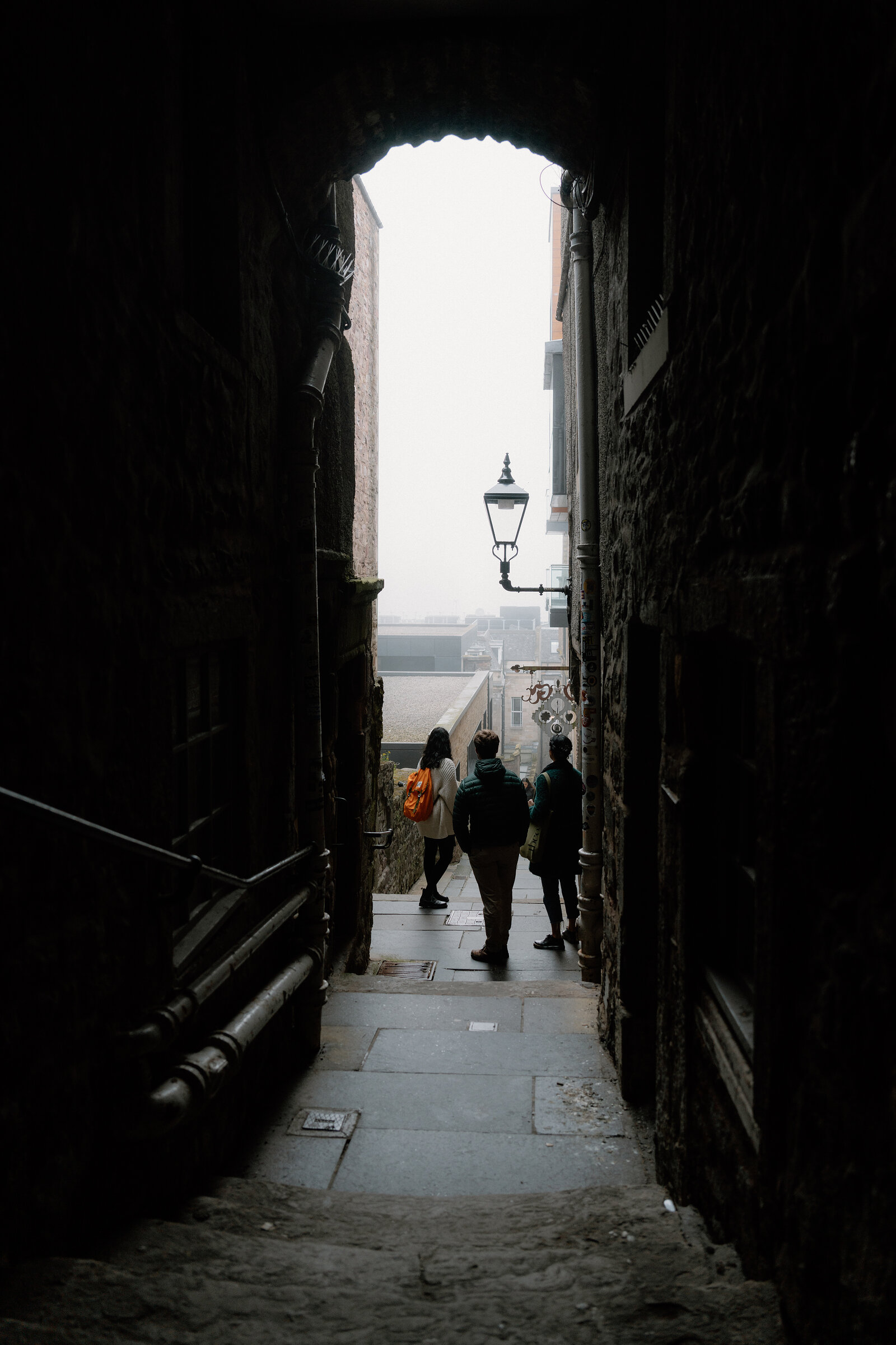 An archway framing a close where pedestrians walk beneath a hanging lamp