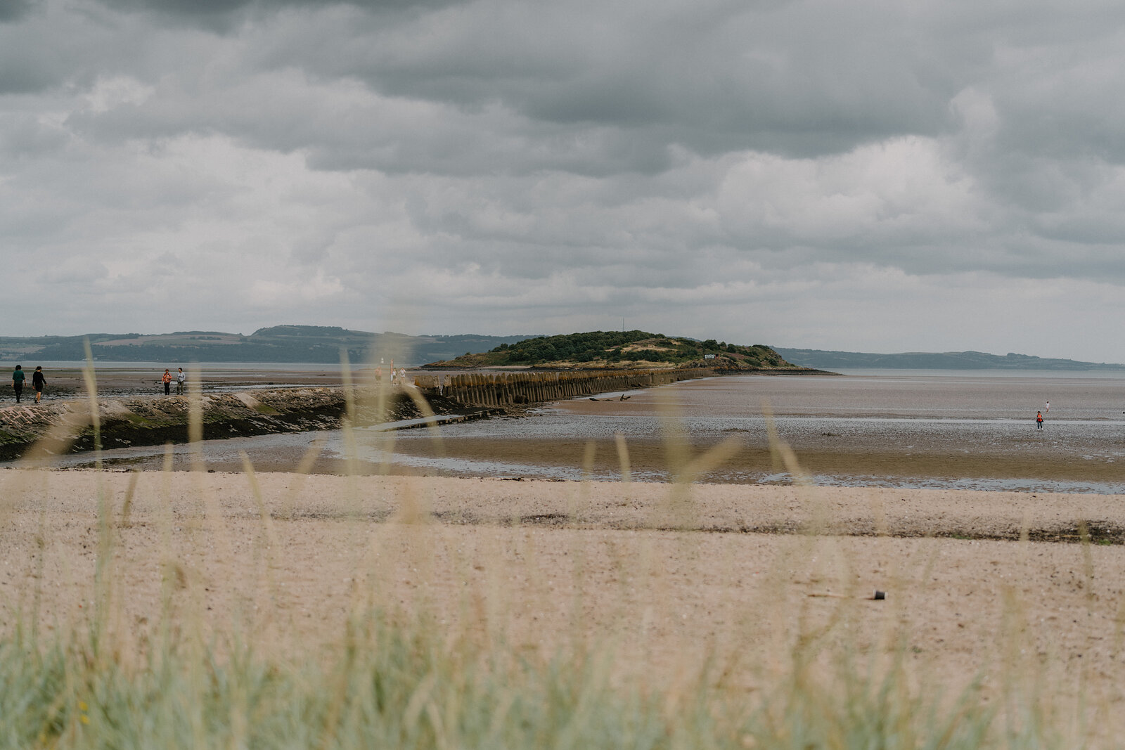 Crammond Beach stretches towards a distant island under a heavy grey sky, dune grass framing the sandy foreground.