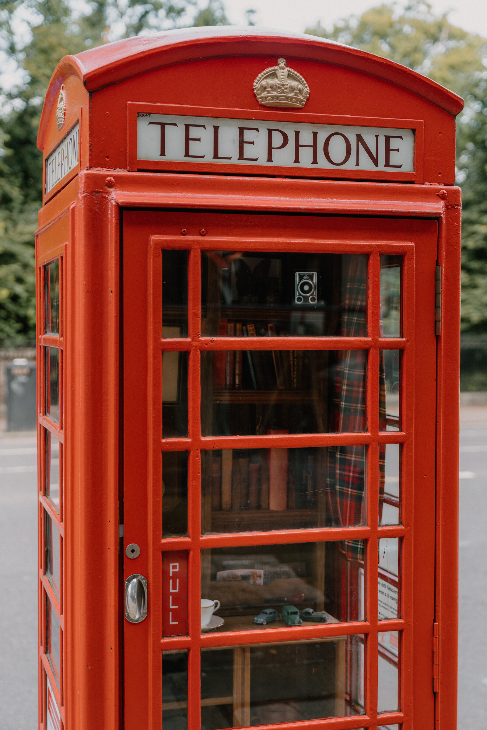 A red telephone box with a crowned Telephone sign, books and a teacup visible inside through the glass